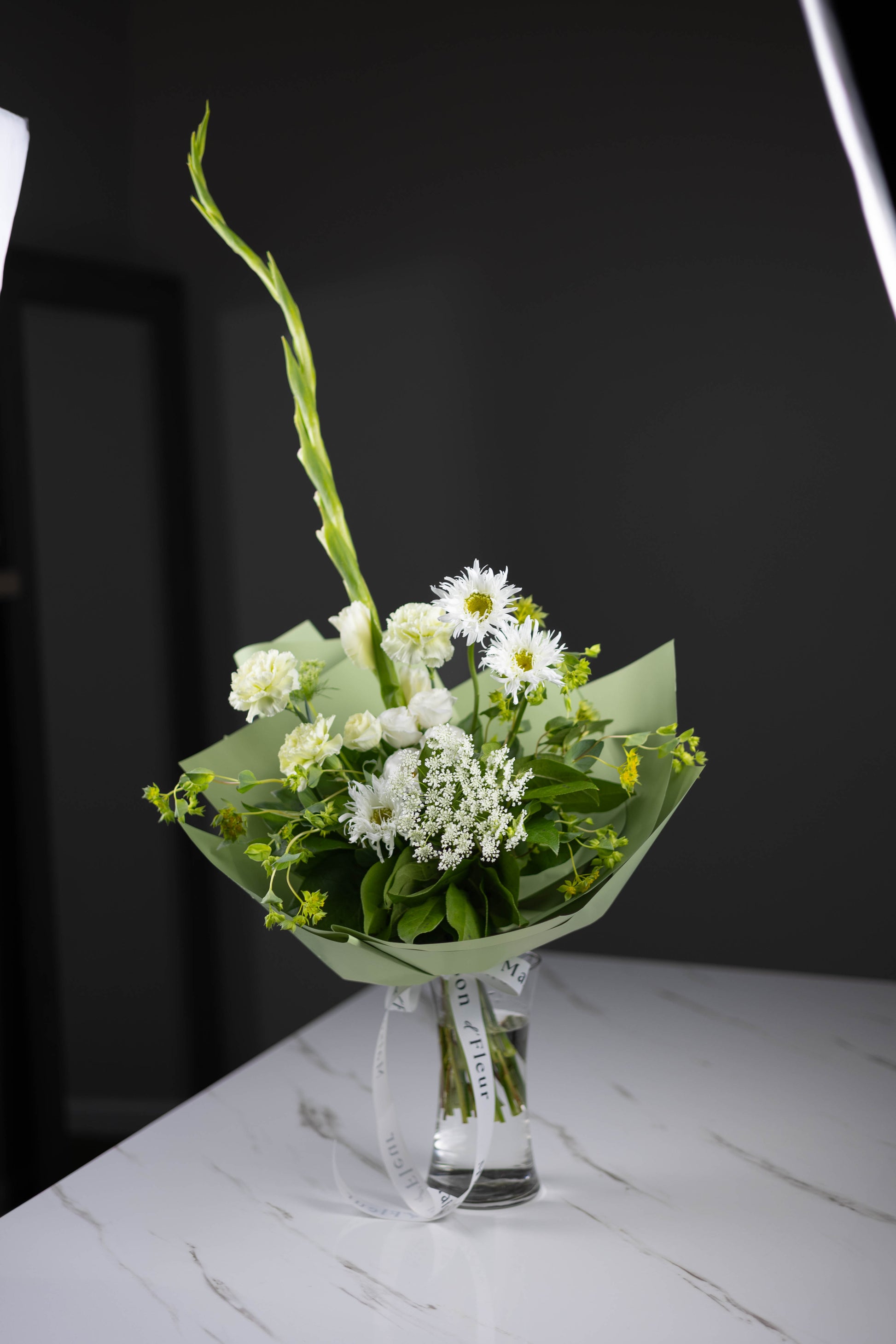 Bouquet of white flowers with green leaves on a marble surface against a black background
