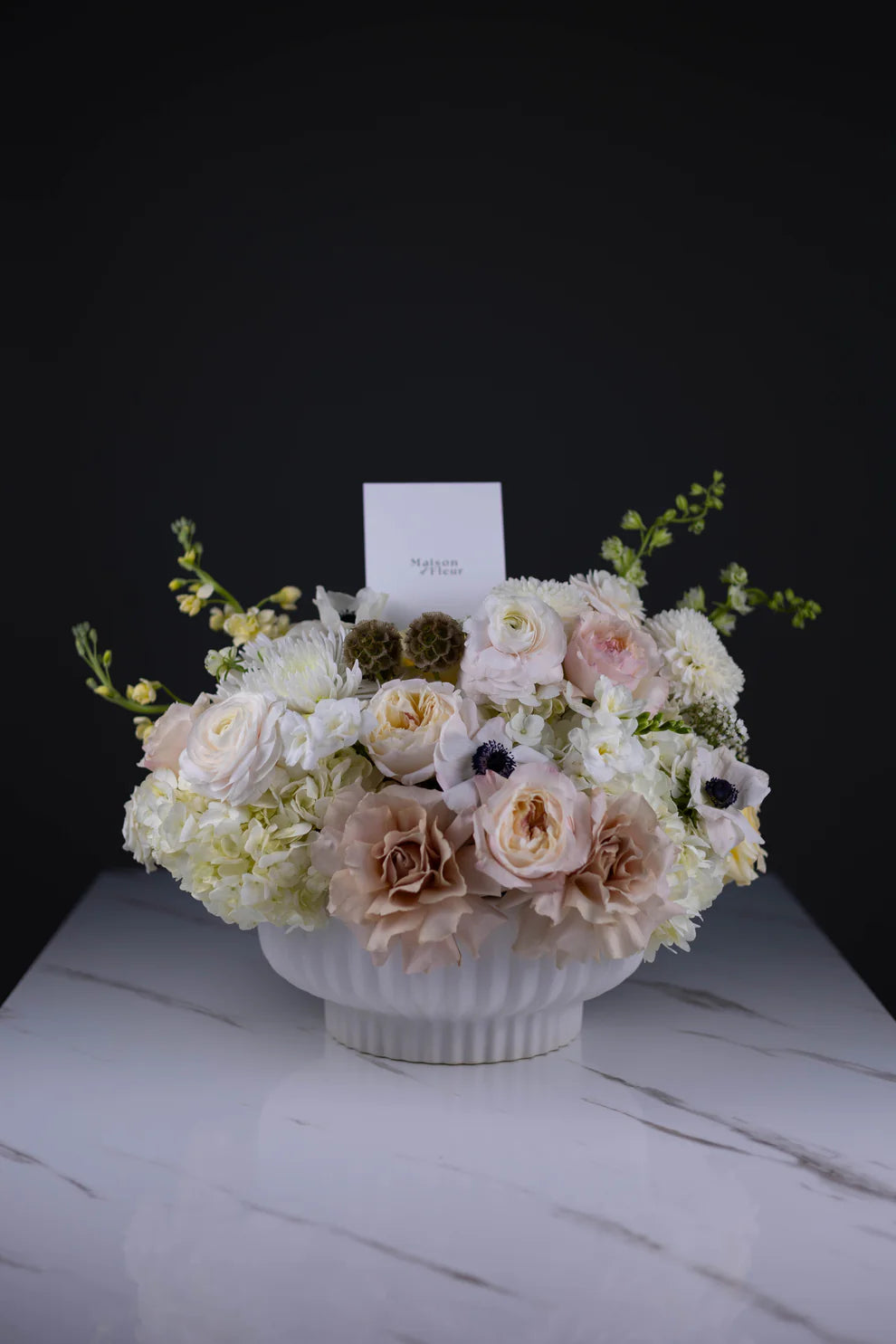 A soft and elegant arrangement in ivory and blush tones, featuring roses, hydrangeas, anemones, and touches of yellow orchids. Set in a classic white vase — refined and timeless.