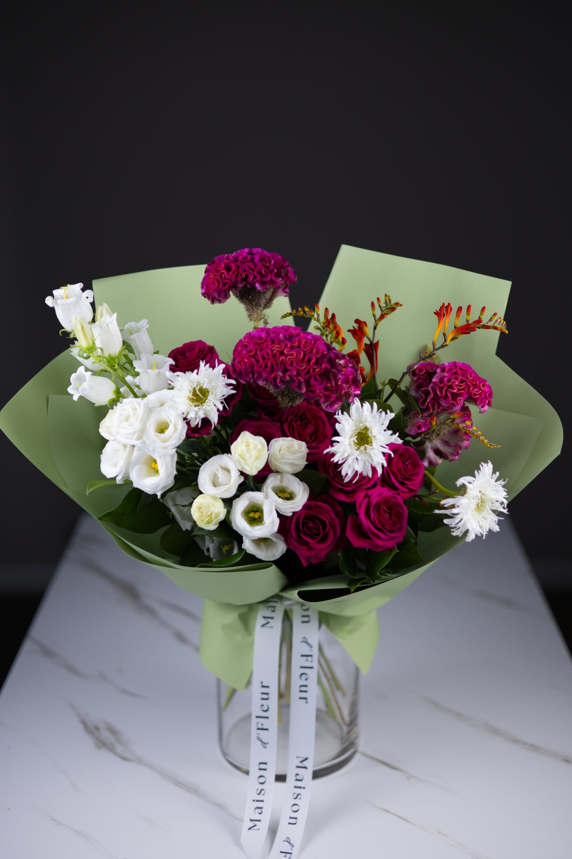 Close-up of a colorful bouquet featuring rich magenta cockscomb, crisp white lisianthus, and fuchsia roses with green foliage.