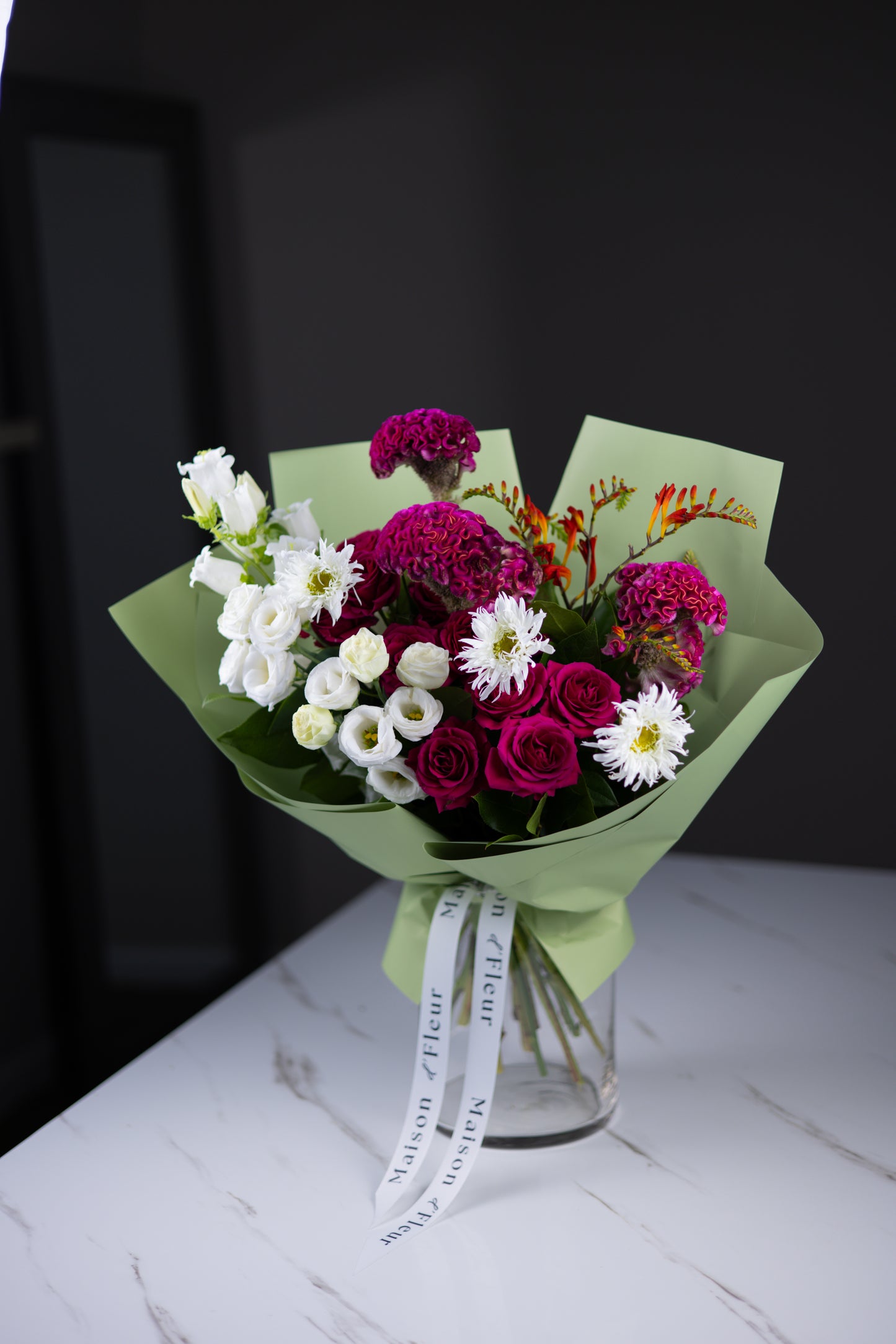 Side view of a striking garden-style bouquet in green wrap, showing the bright mix of deep pink, white, and orange blooms.