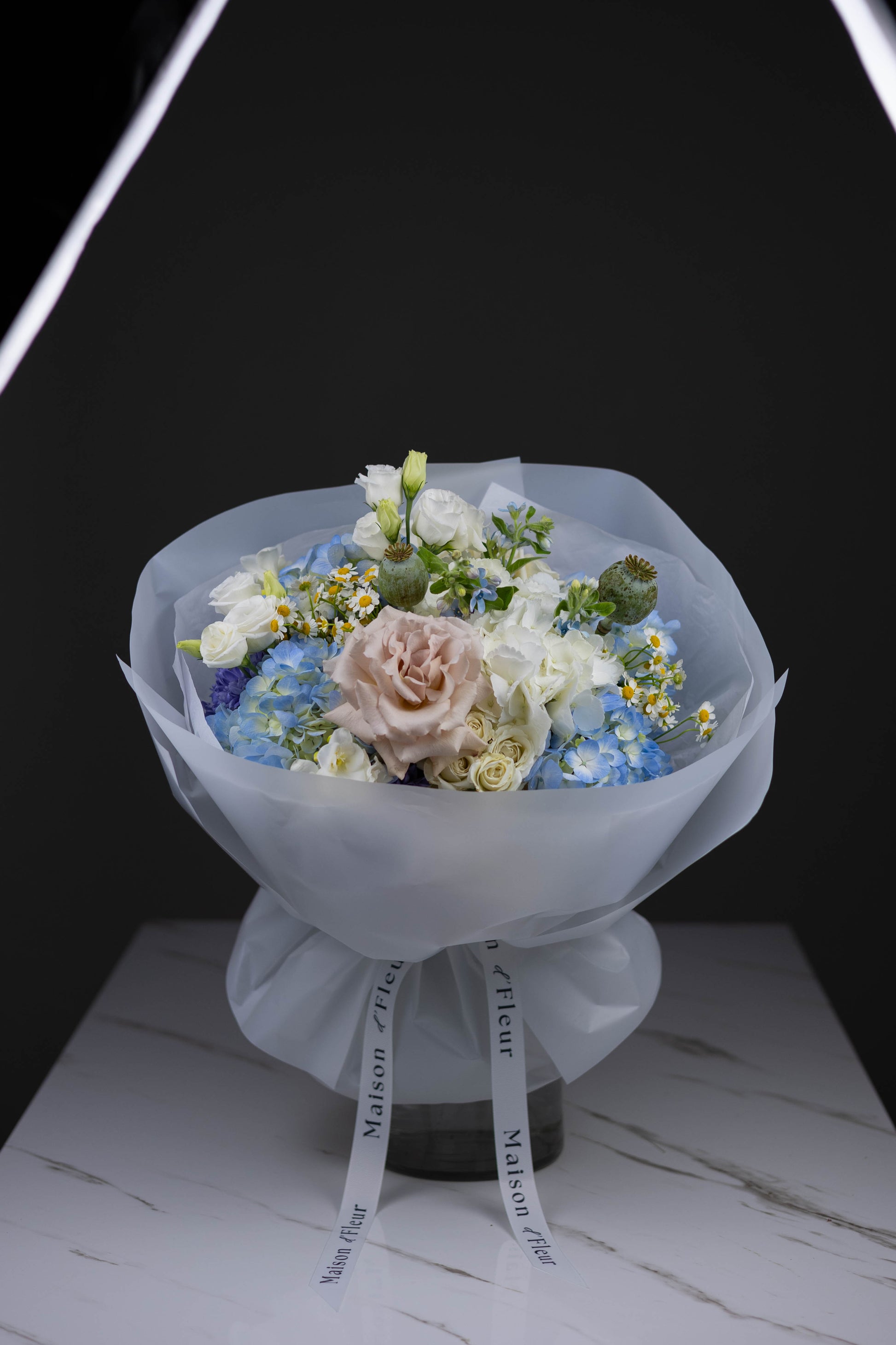 A dreamy blend of pastel blush roses, creamy florals, and striking blue hydrangeas — all wrapped in a soft, cloud-like paper with signature Maison d’Fleur ribbons. This bouquet feels like a quiet morning or a soft-spoken “I love you.” Perfect for birthdays, thank-you gifts, or just because.