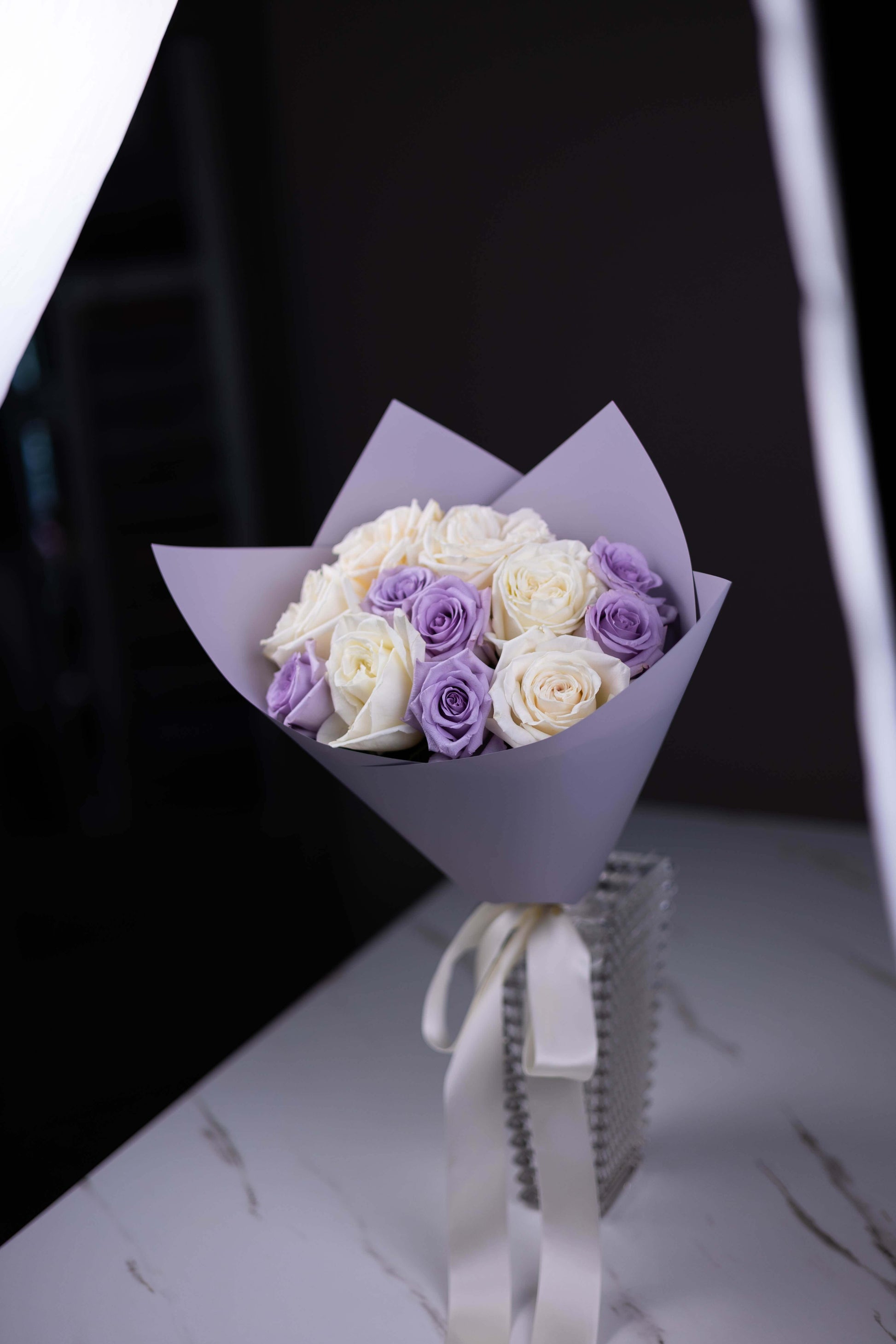 Bouquet of white and purple roses wrapped in paper with a ribbon on a dark background