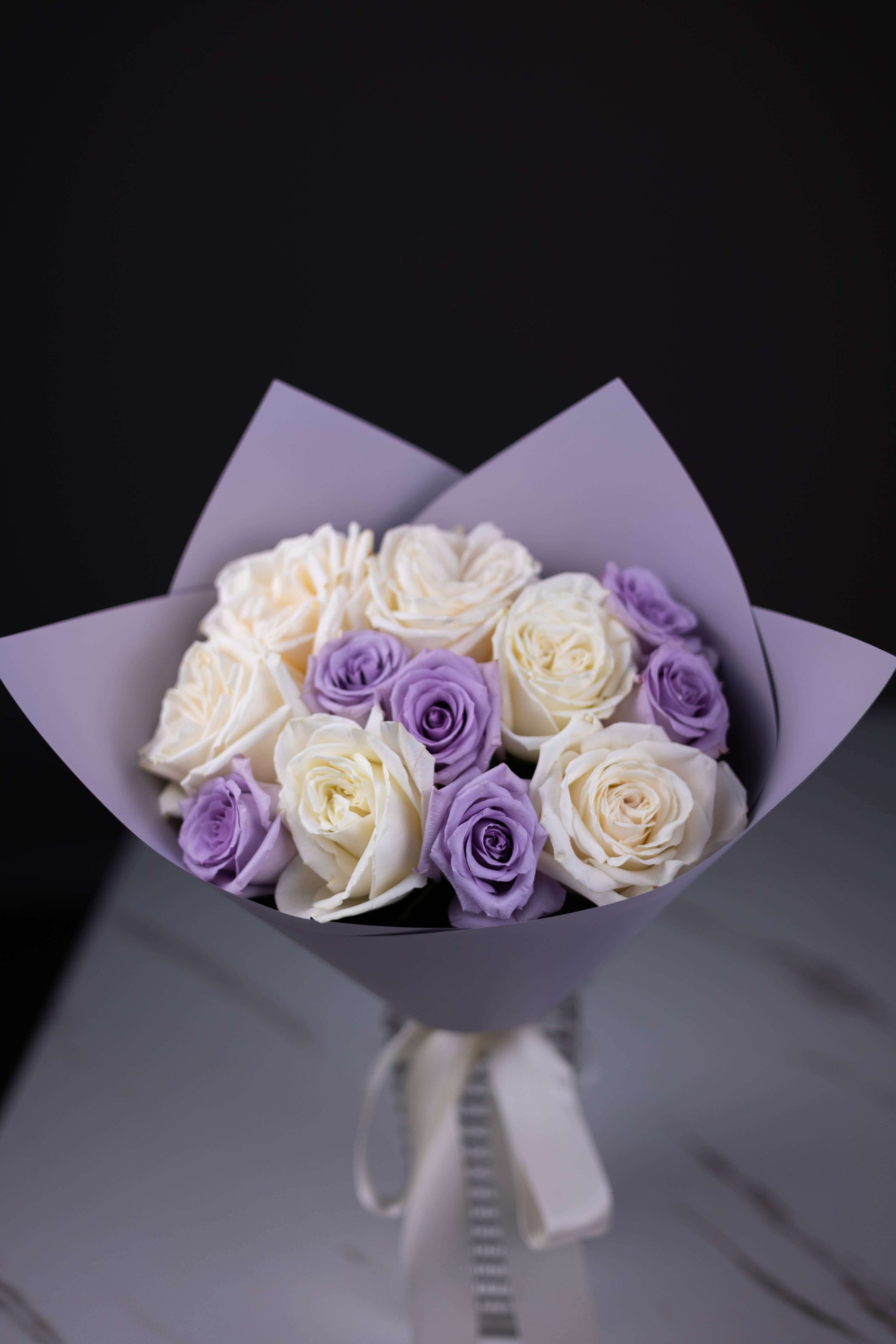 Bouquet of white and purple roses wrapped in purple paper on a dark background