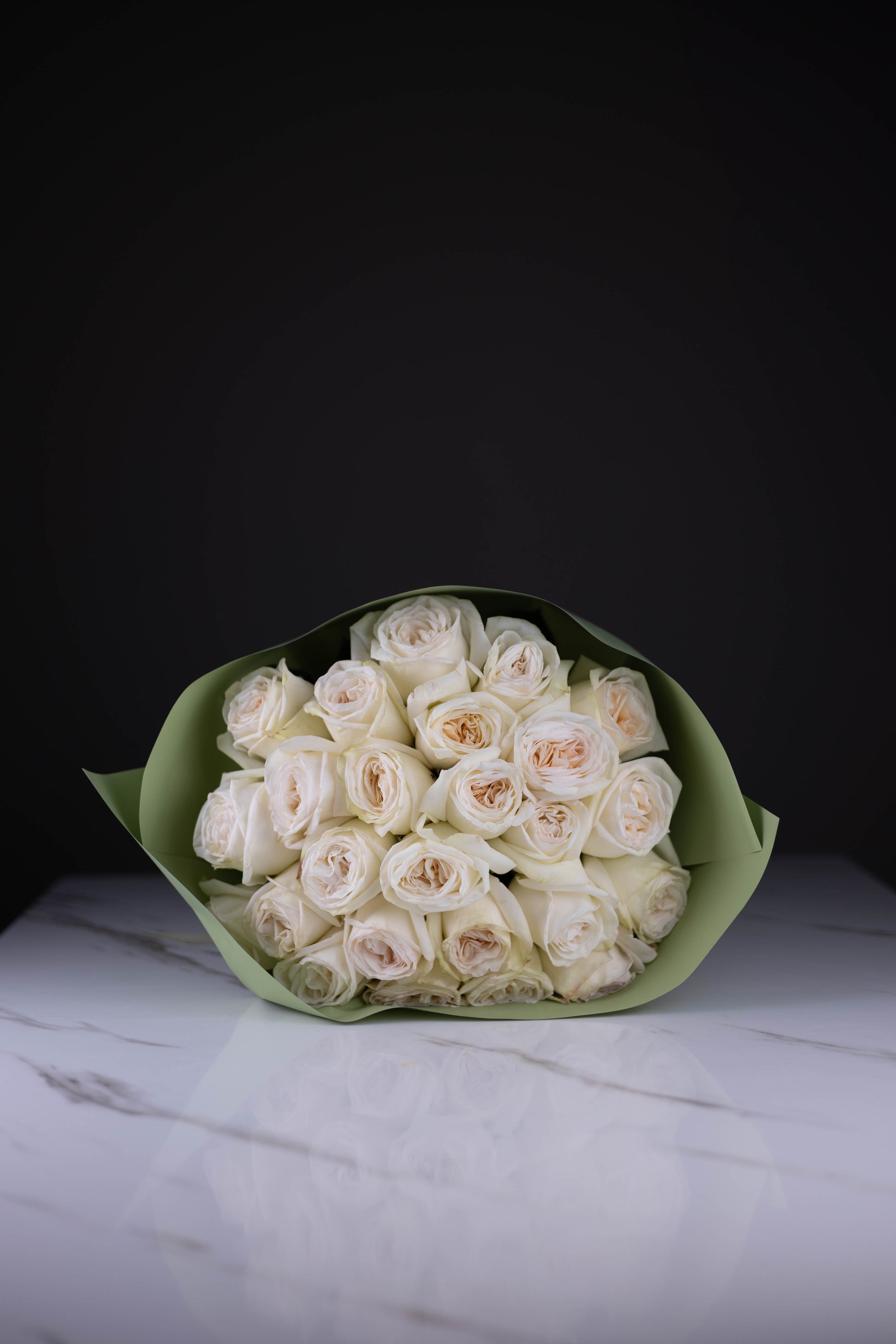 Bouquet of white roses wrapped in green paper on a marble surface with a black background