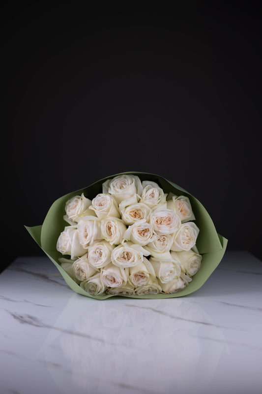 Bouquet of white roses wrapped in green paper on a marble surface with a black background