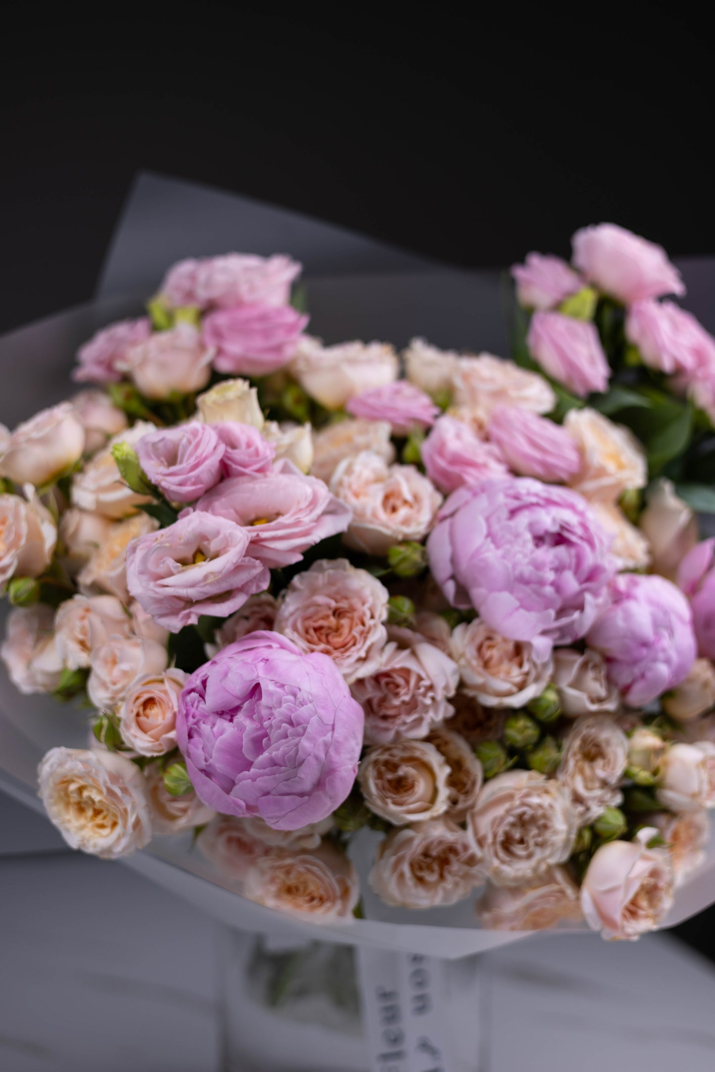 Close-up of a romantic bouquet showing pink peonies and peach-toned spray roses in delicate layers.