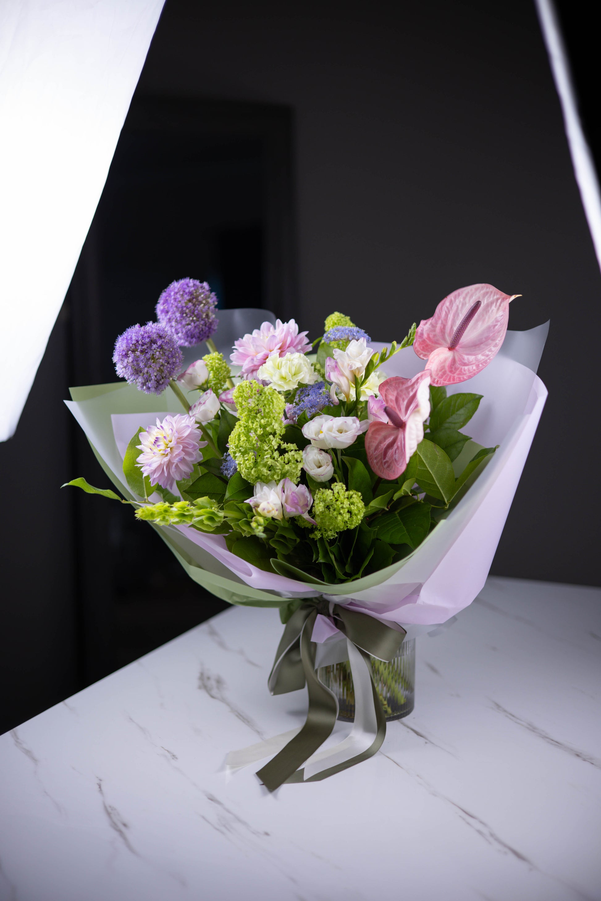 Full view of Fleur de Rêve bouquet in pastel wrap with satin ribbon on a table
