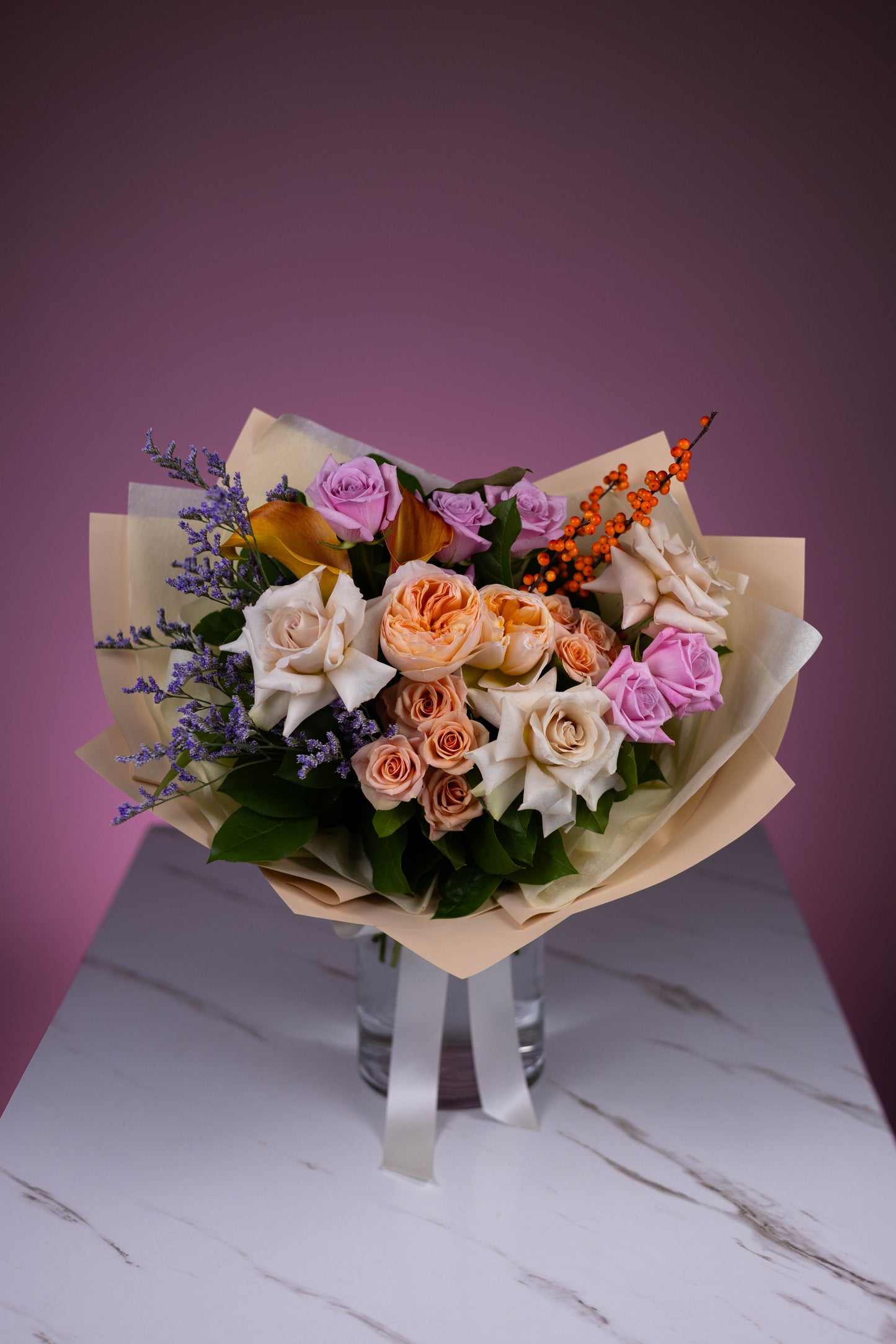 Full view of a Maison d’Fleur bouquet wrapped in cream paper with peach, lavender, and white florals in a glass vase