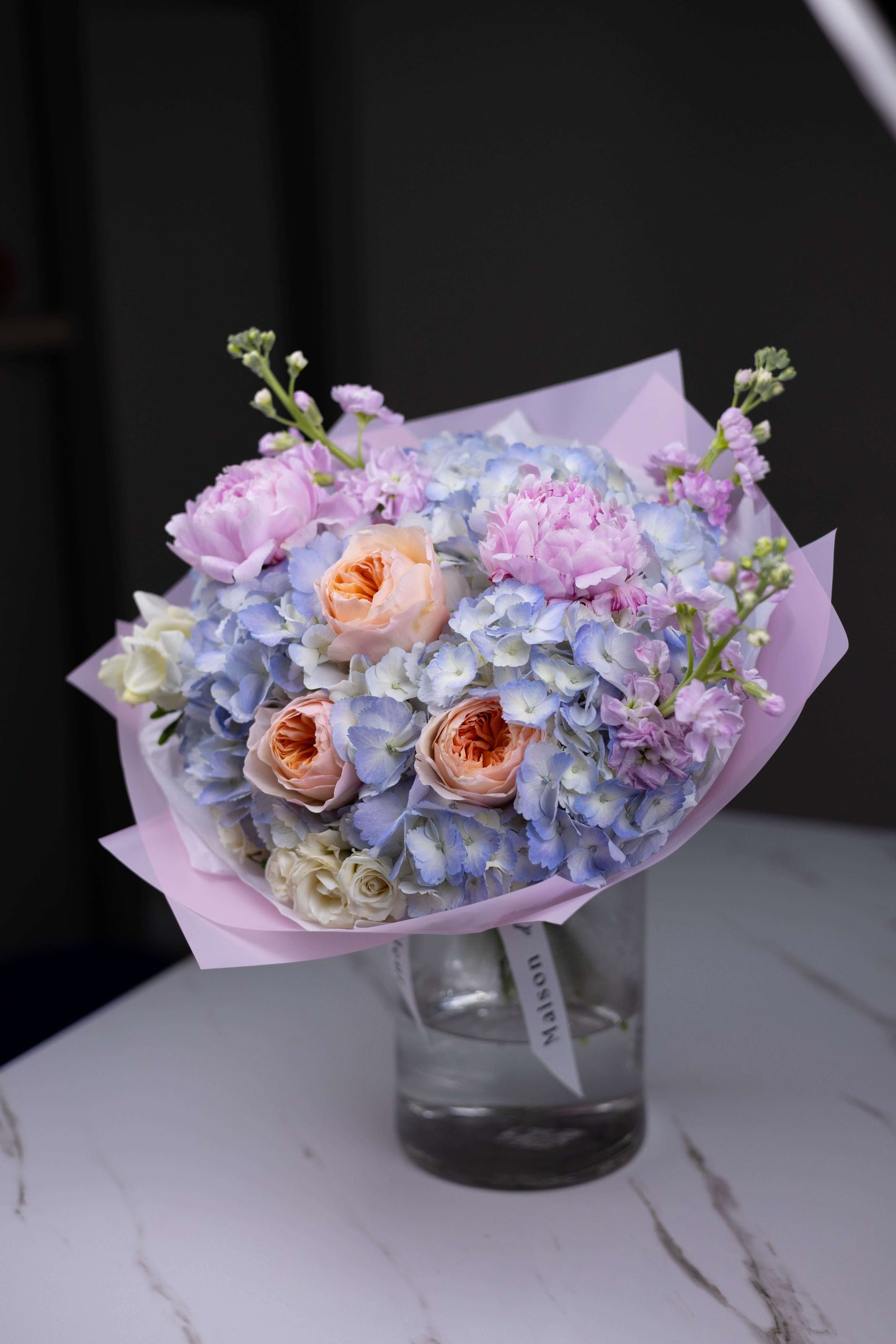 Artistic bouquet of soft peach roses and pastel blooms in glass vase by Maison d’Fleur boutique