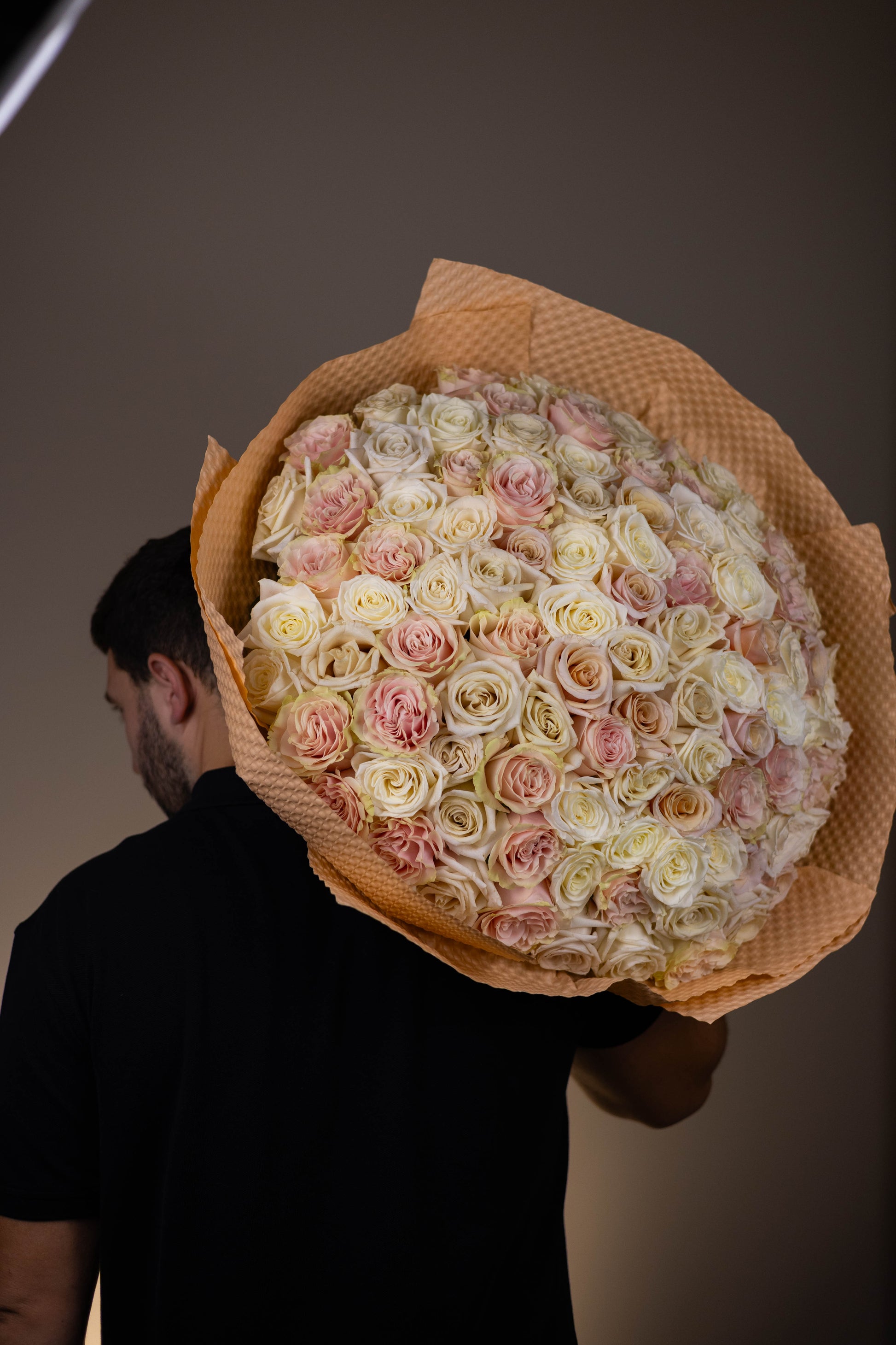 Person holding a large bouquet of white and pink roses against a plain background