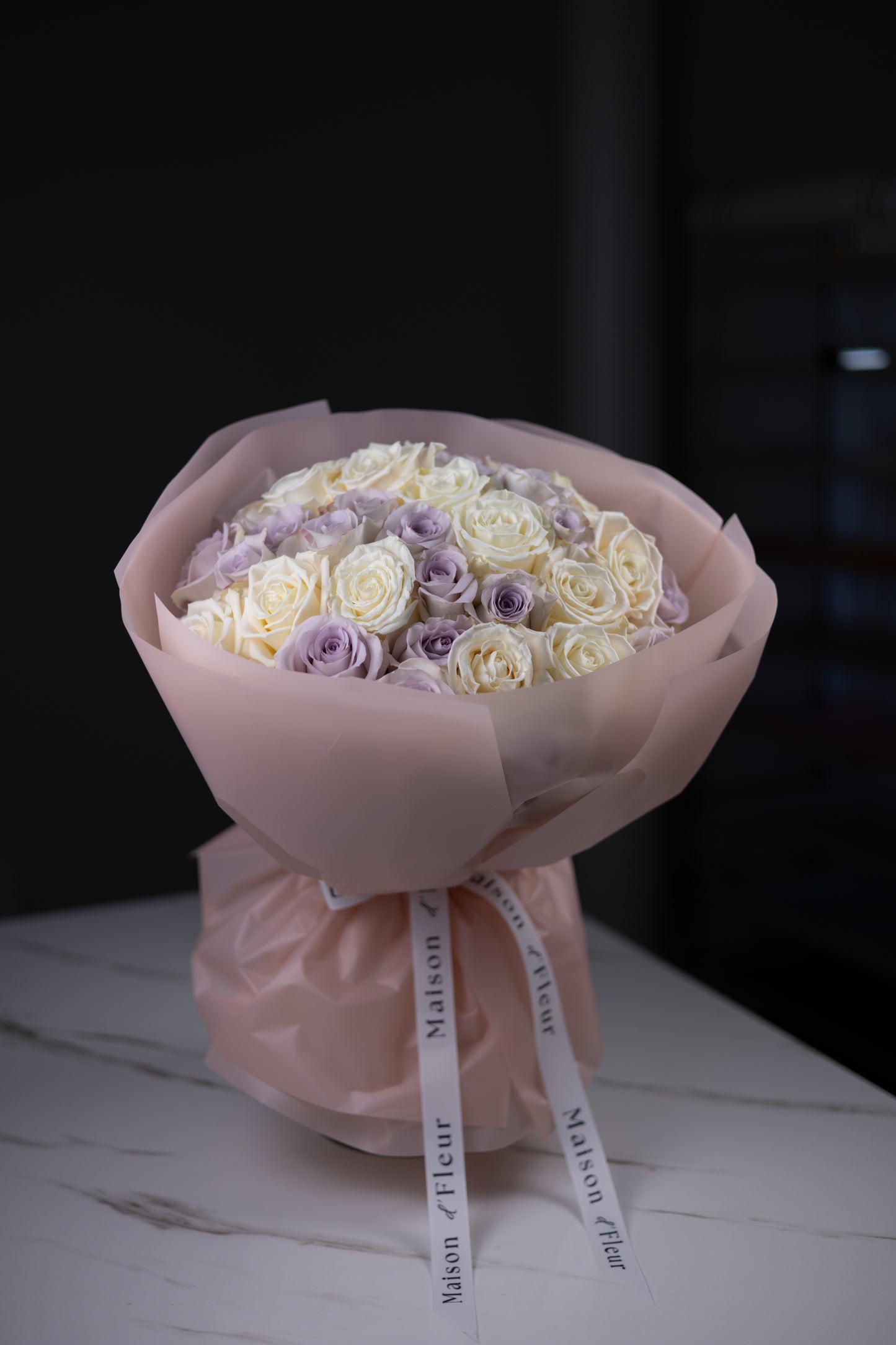 Close-up angled view of a pastel bouquet of ivory and lavender roses in blush wrapping.