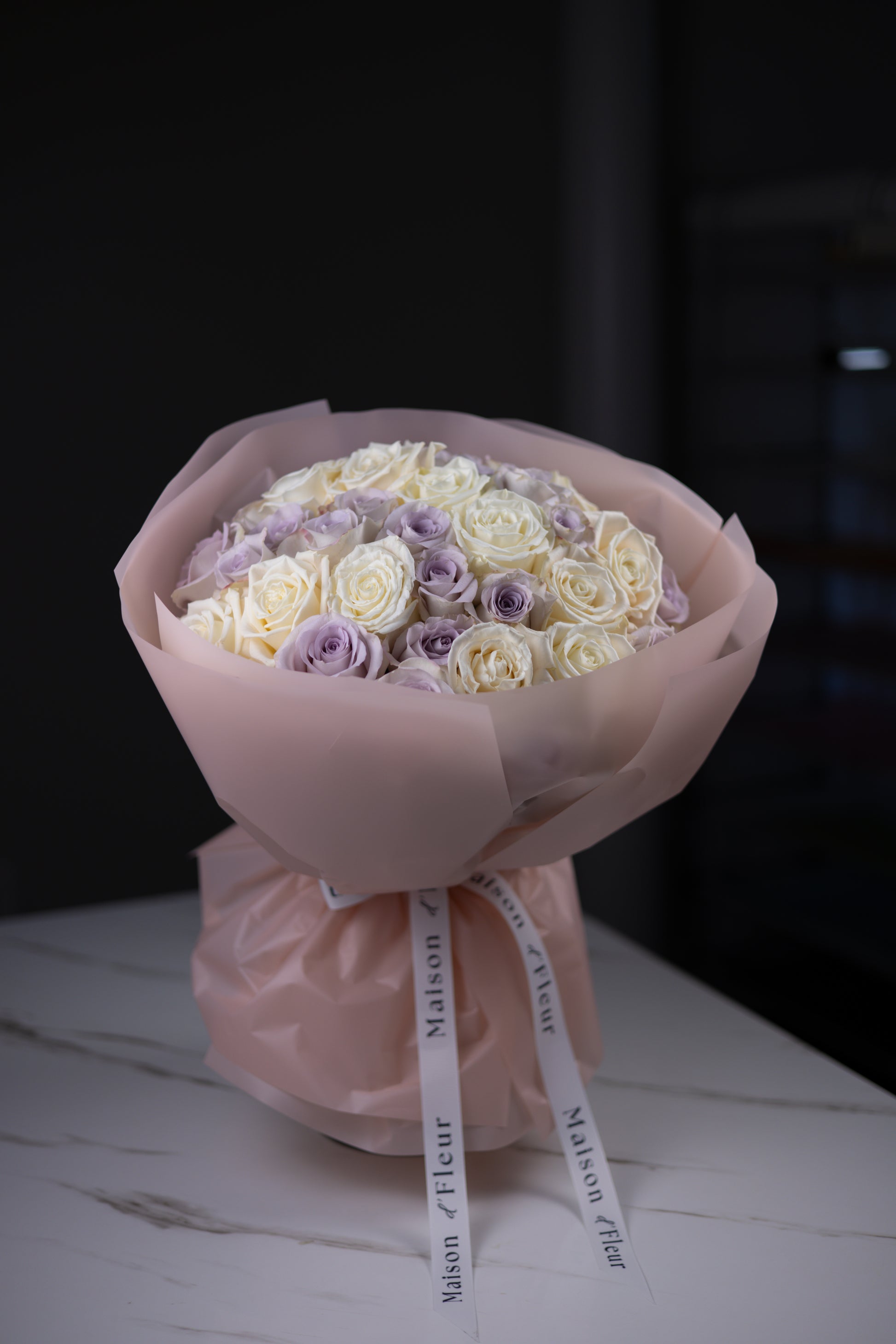 Close-up angled view of a pastel bouquet of ivory and lavender roses in blush wrapping.