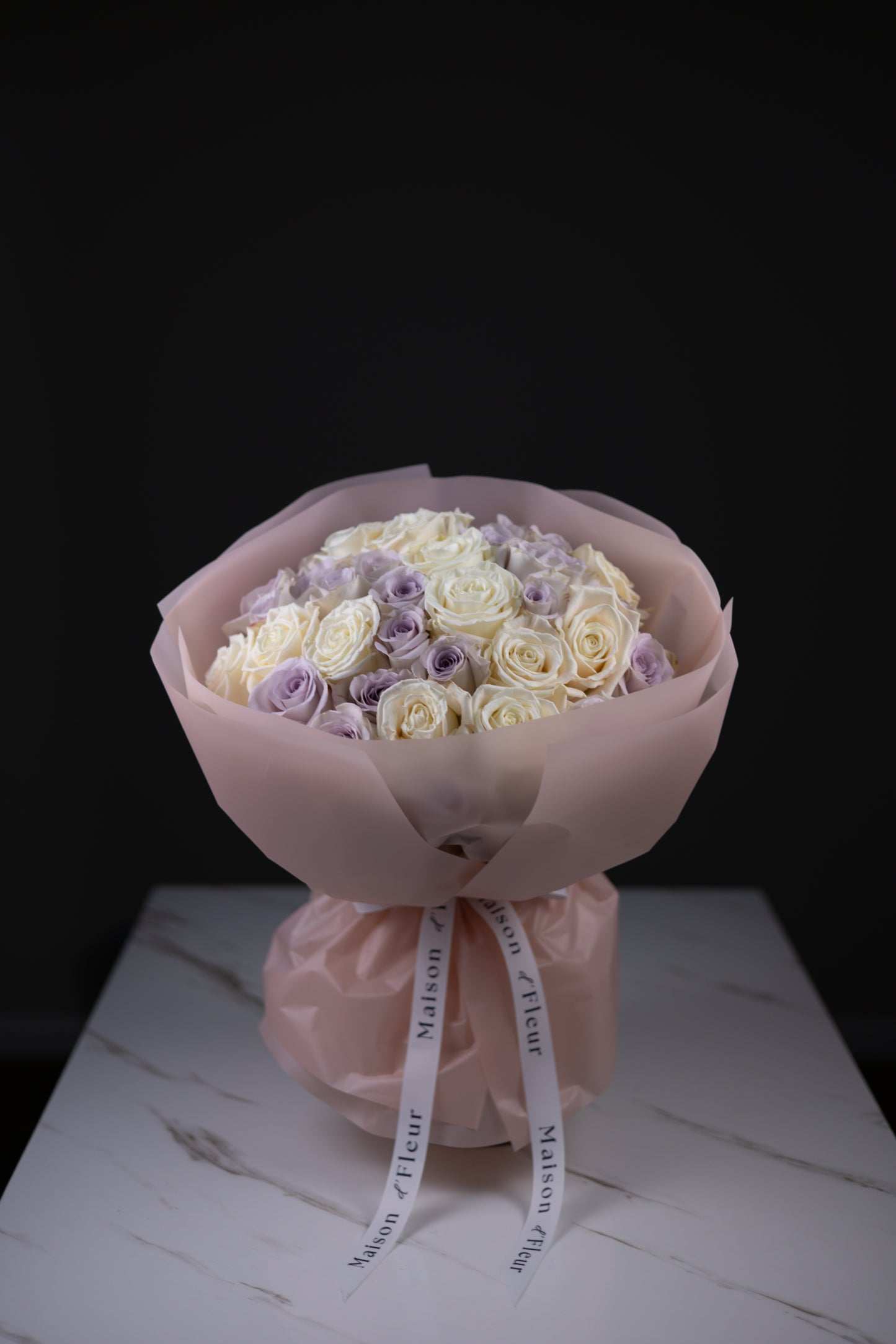 Bouquet of white and purple roses wrapped in pink paper with a ribbon on a dark background