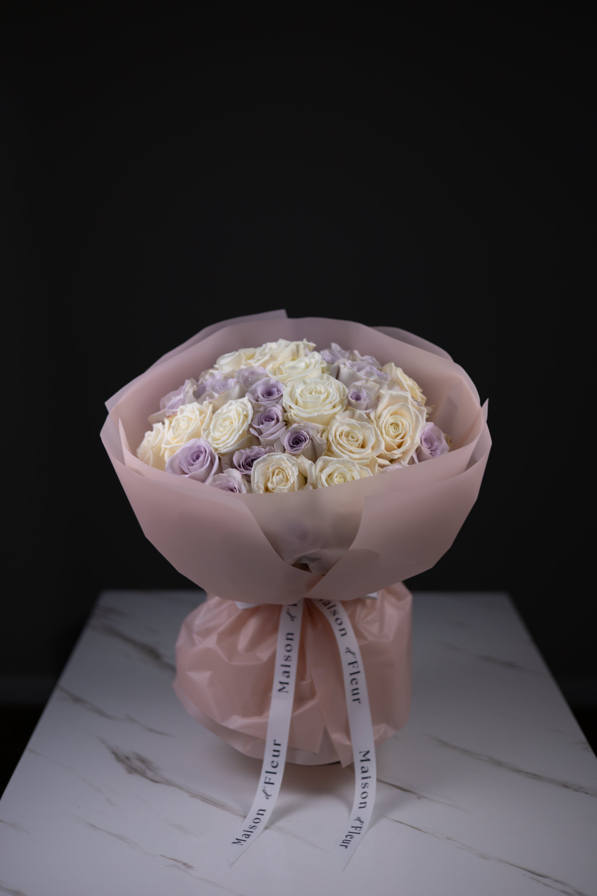 Bouquet of white and purple roses wrapped in pink paper with a ribbon on a dark background
