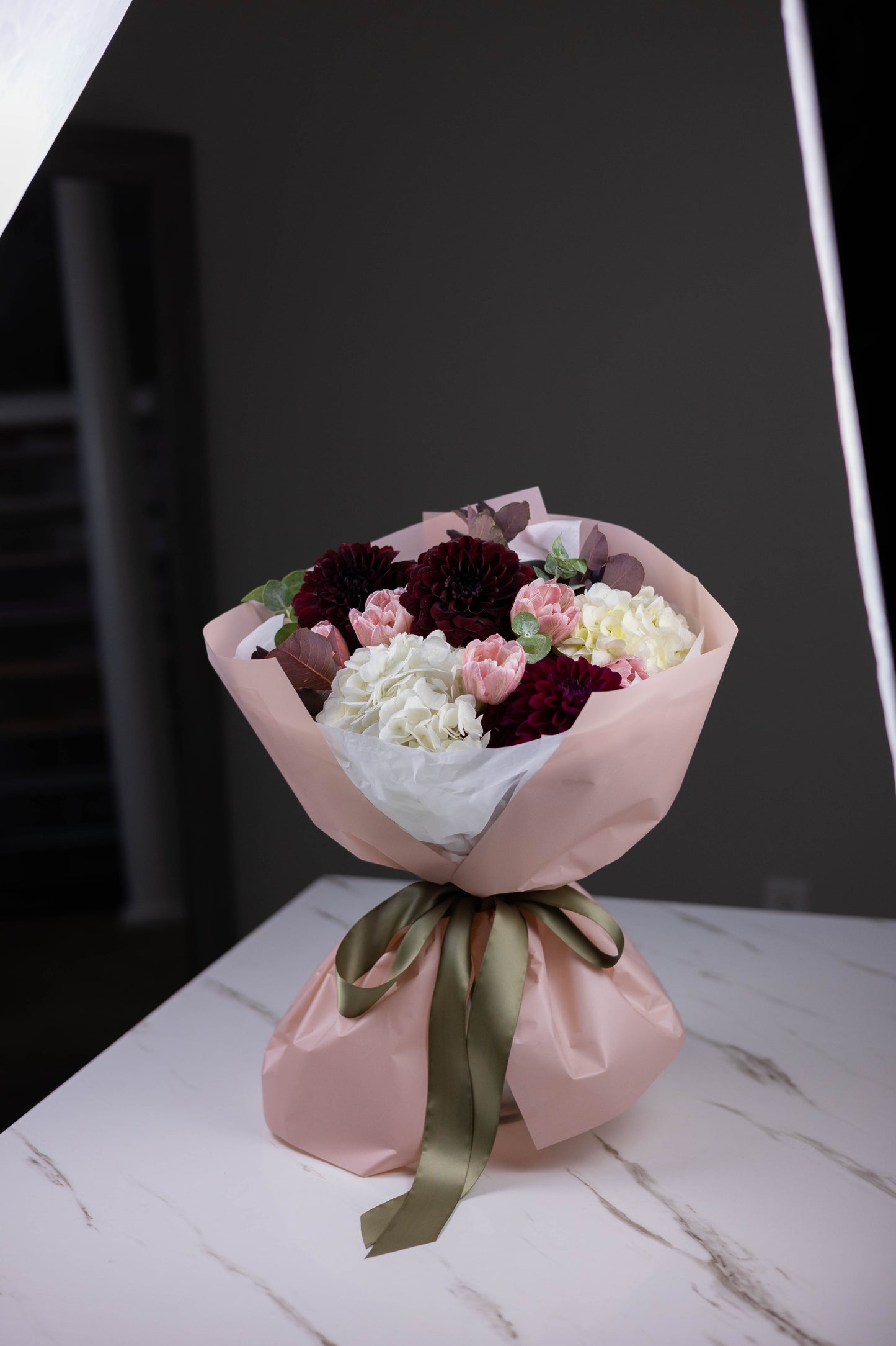 Bouquet of flowers wrapped in pink paper with a green ribbon on a marble surface.