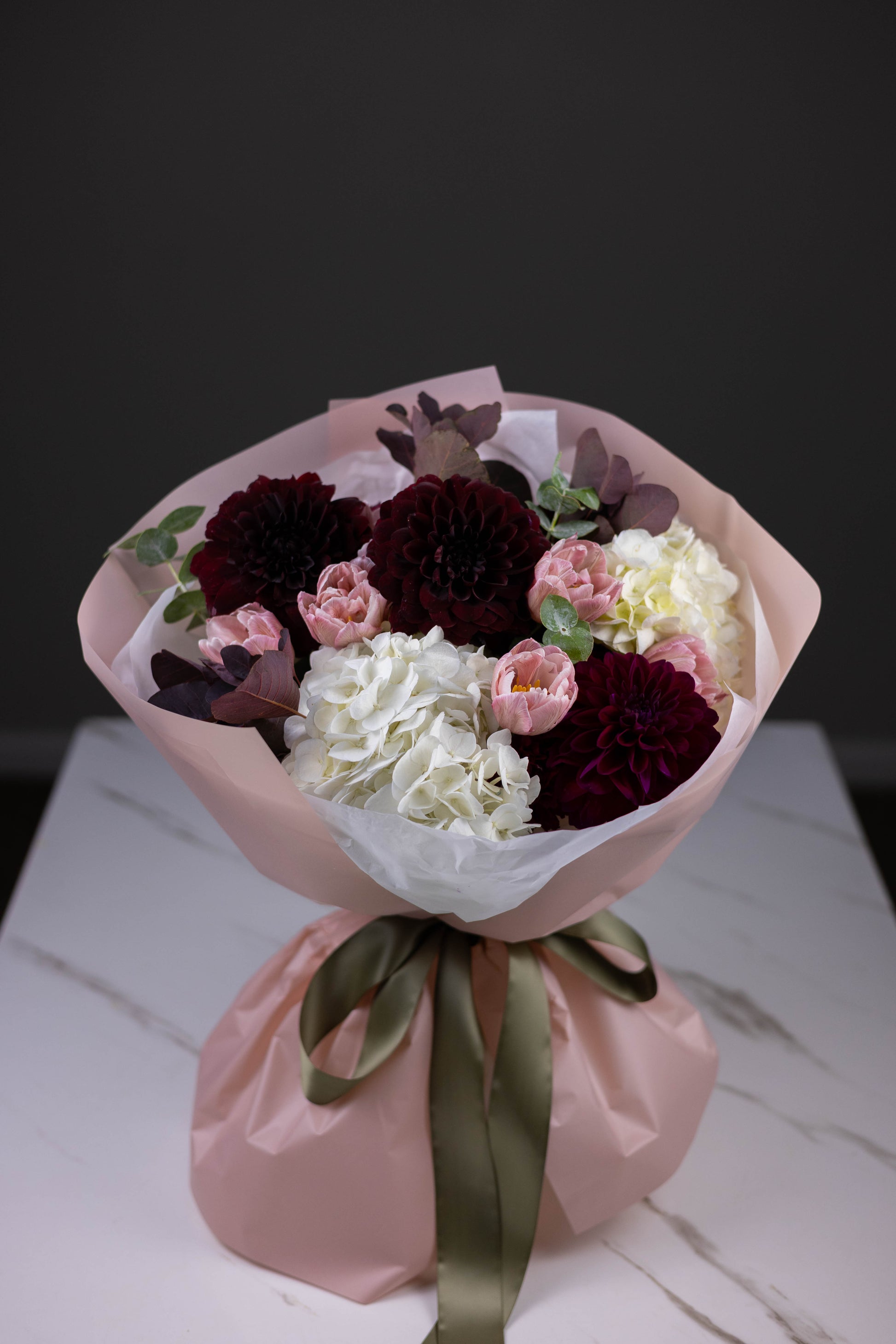 Bouquet of flowers wrapped in pink paper with a green ribbon on a white surface.
