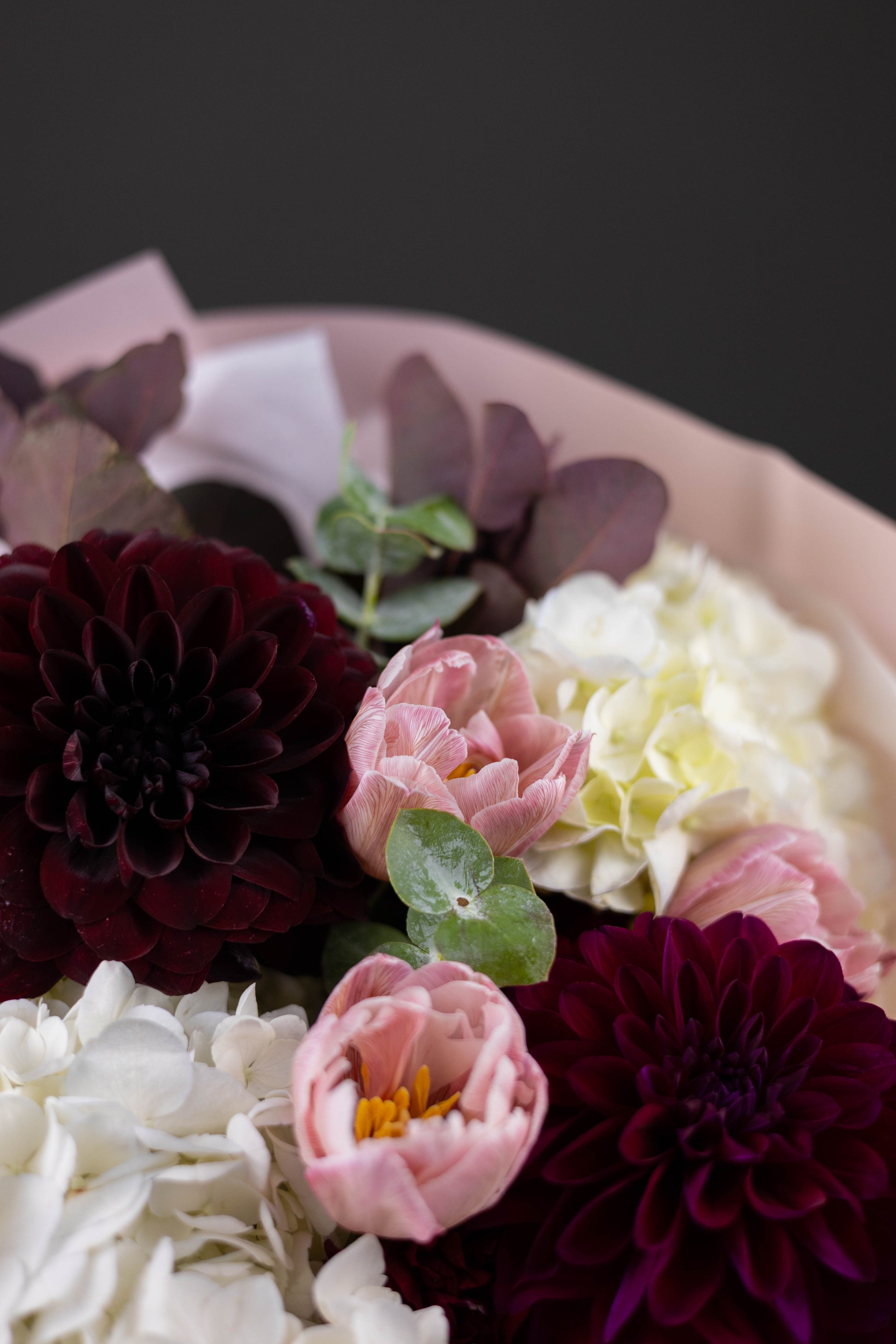 Close-up of a bouquet of flowers with dark purple, pink, and white colors on a dark background.
