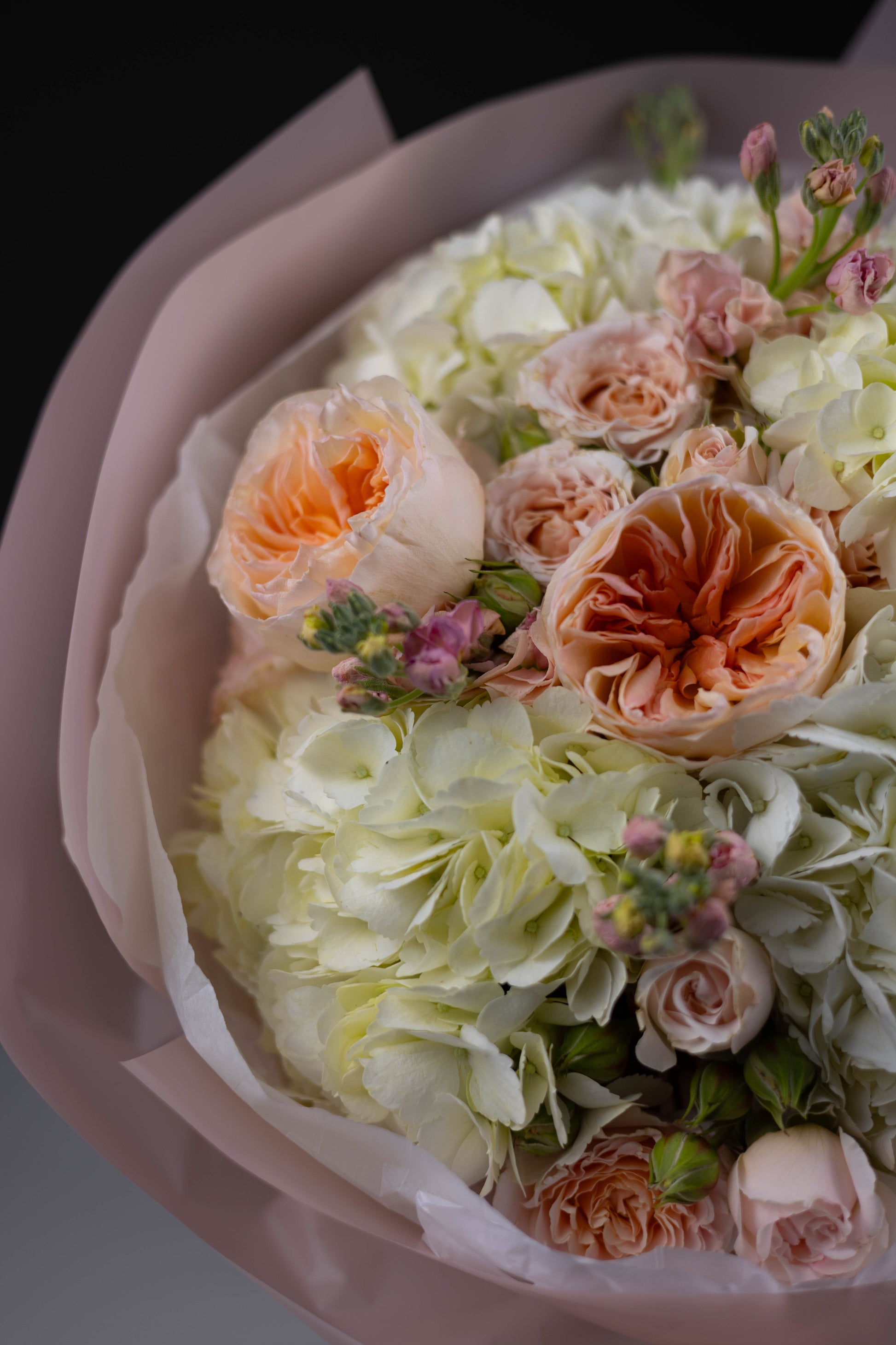 Top view of a soft and romantic floral bouquet with creamy white and peach tones, featuring hydrangeas, garden roses, and sprigs of stock.