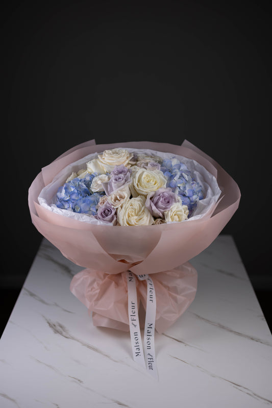 Pastel floral bouquet with roses and hydrangeas displayed on a marble table.