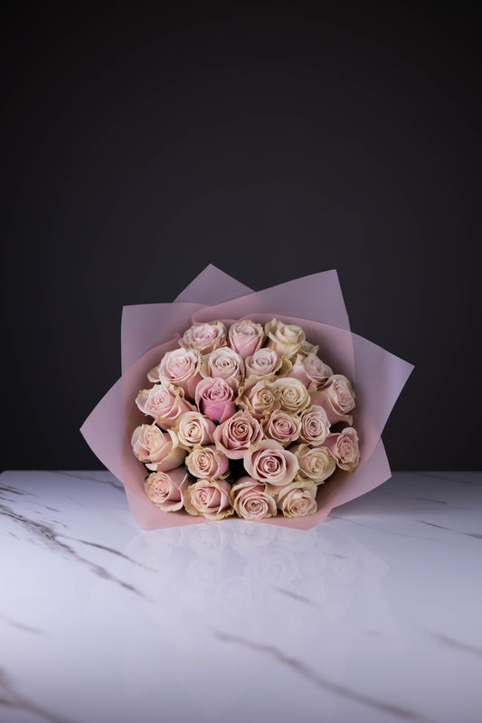 Elegant bouquet of blush pink roses wrapped in soft pink paper, placed on a white marble table.