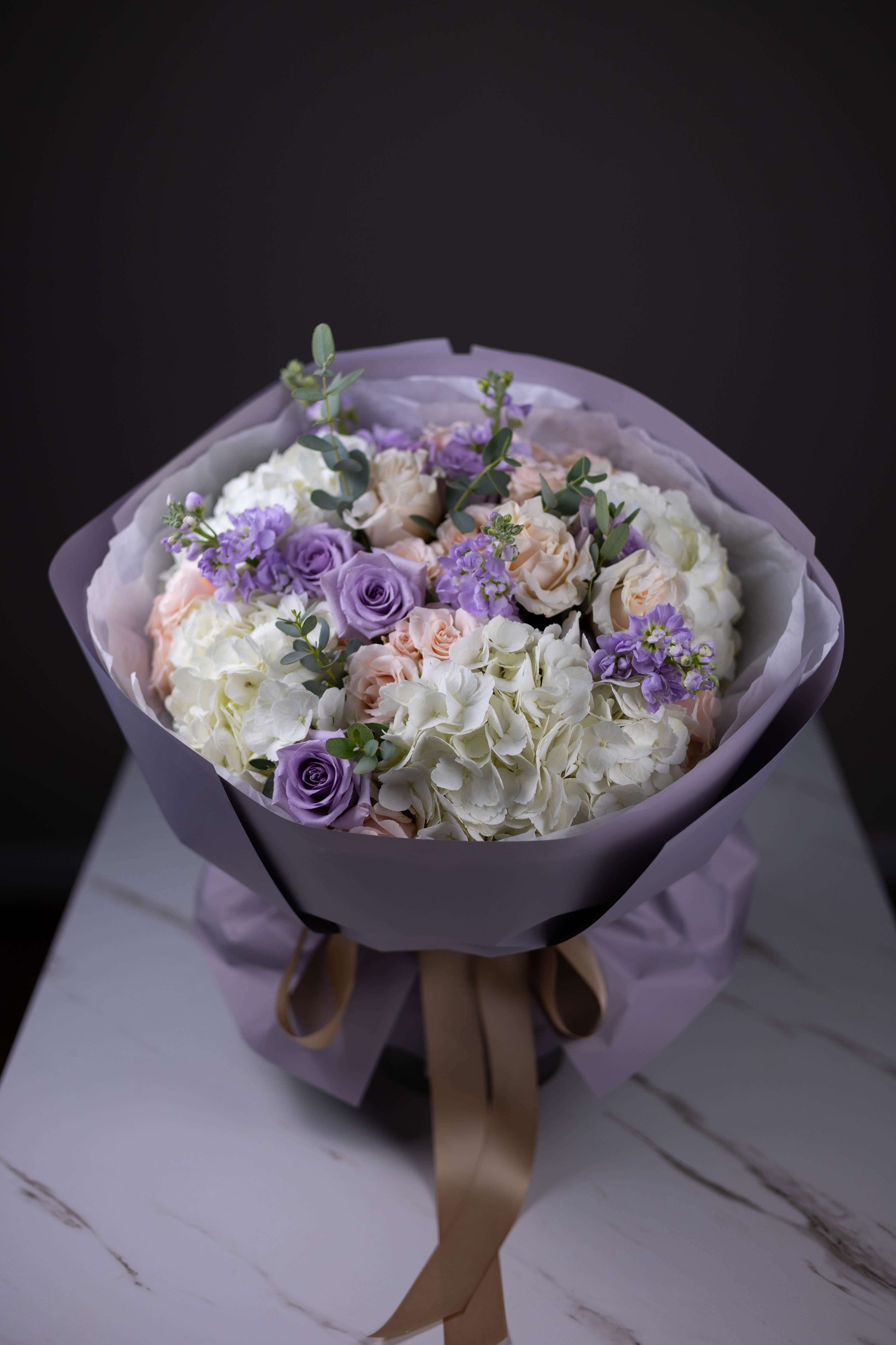 Bouquet of flowers with purple and white flowers wrapped in purple paper on a dark background