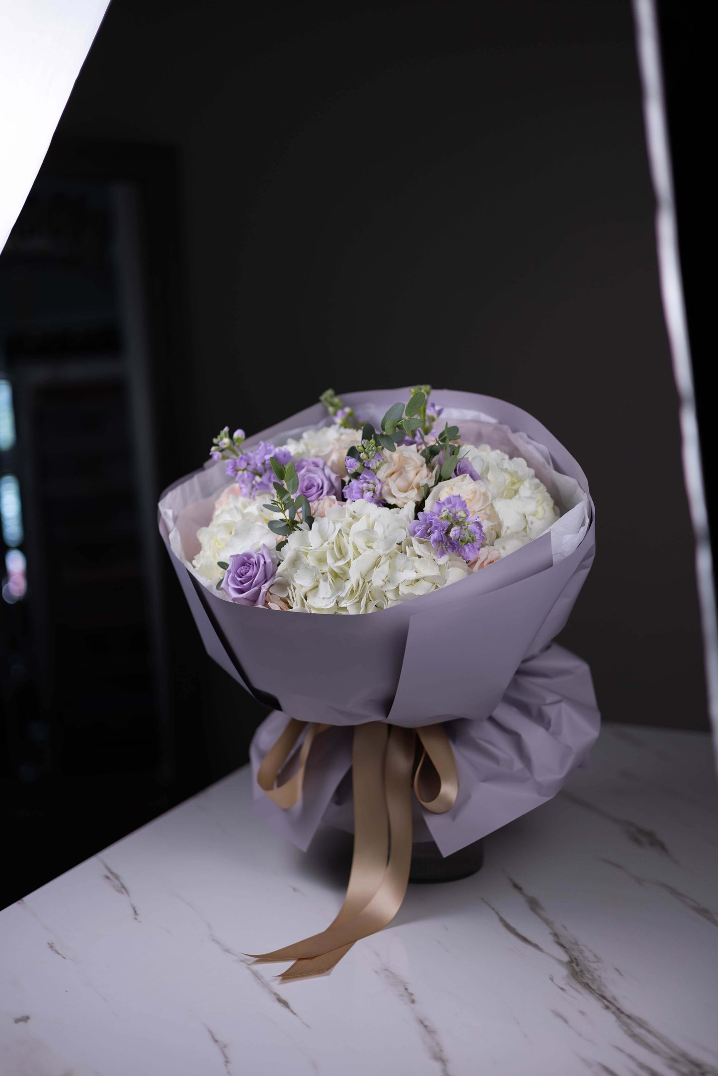 Bouquet of flowers wrapped in purple paper with a gold ribbon on a marble surface.