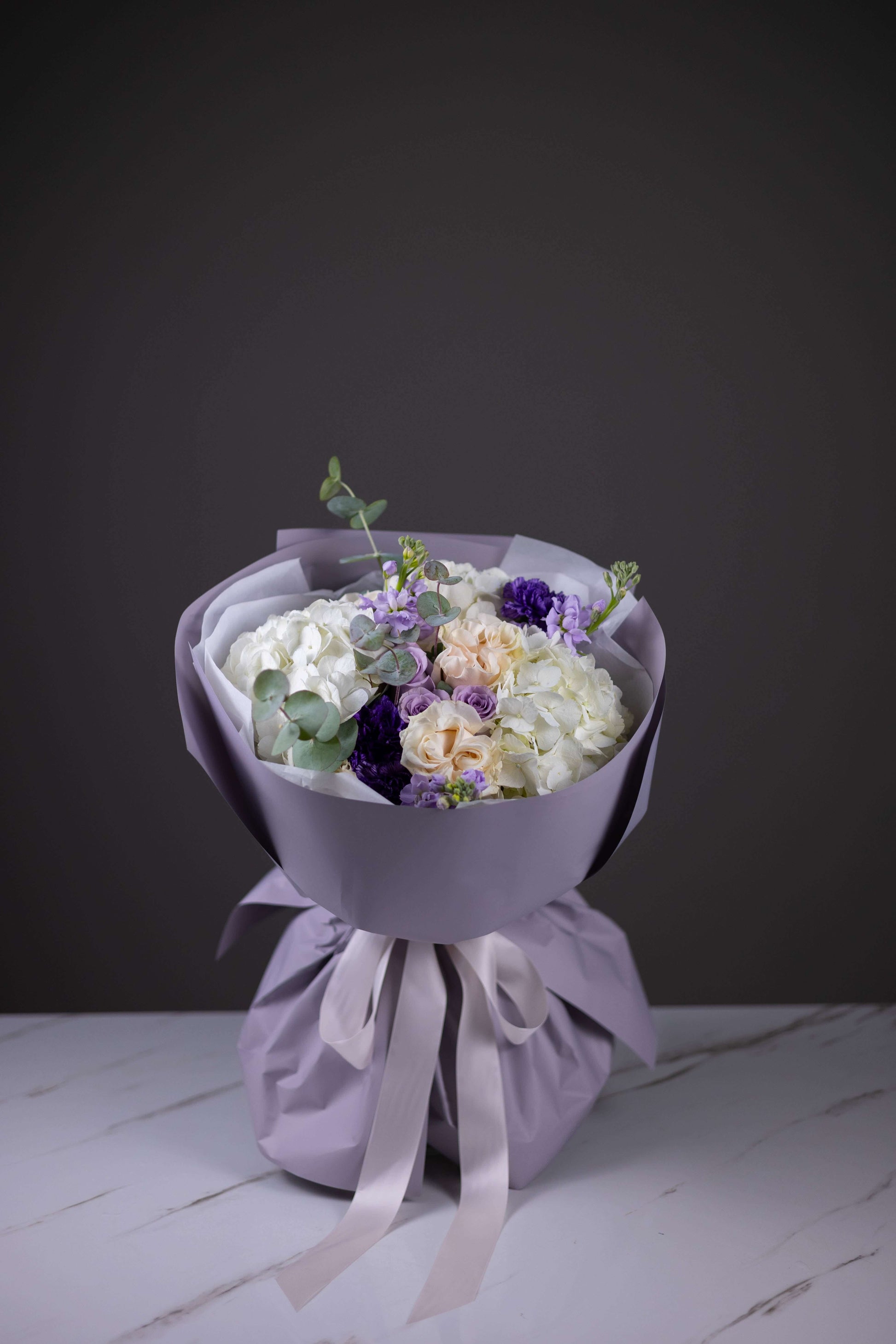 Bouquet of flowers wrapped in purple paper with a white ribbon on a dark background