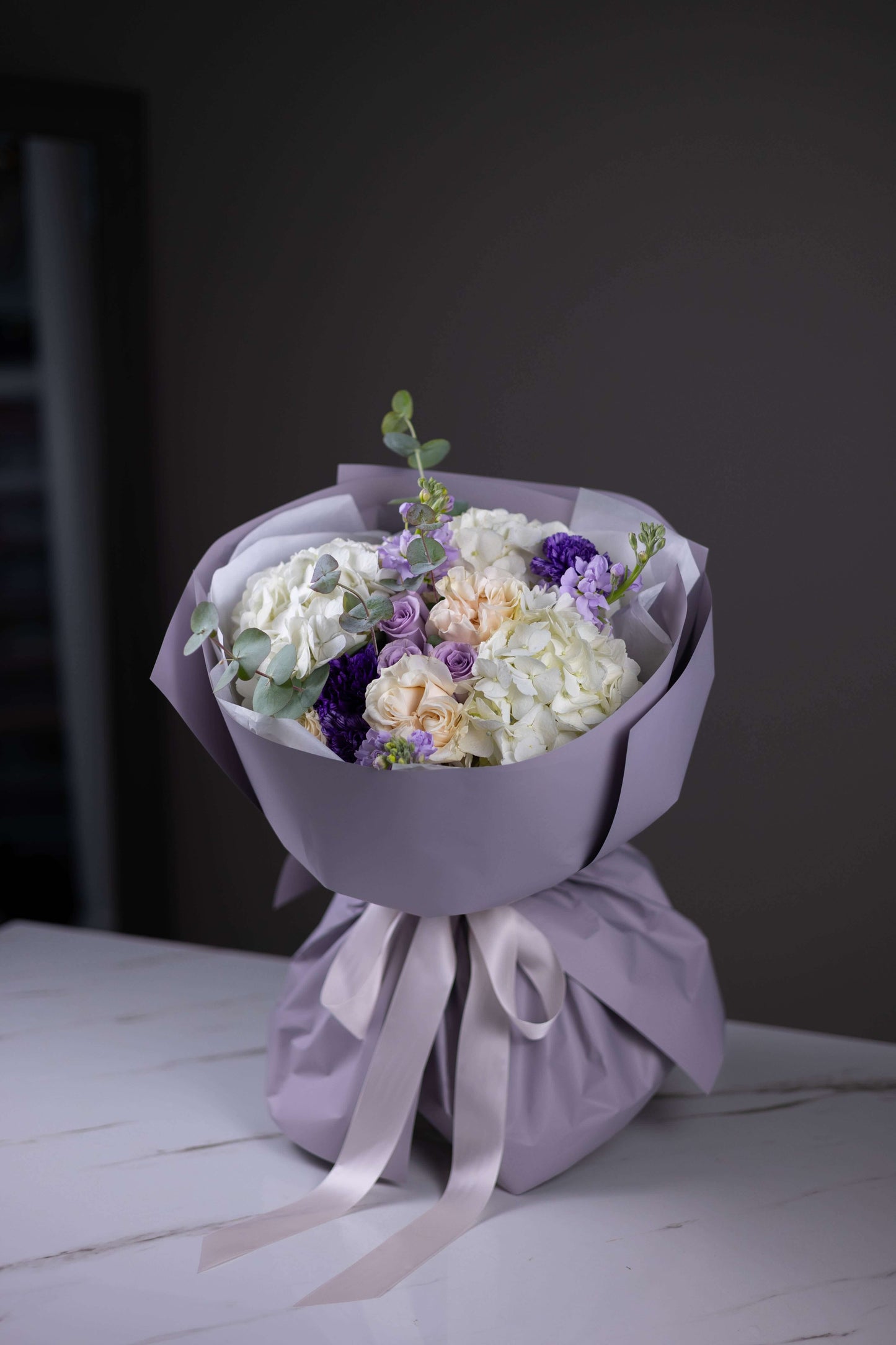Bouquet of flowers wrapped in purple paper with a white ribbon on a dark background