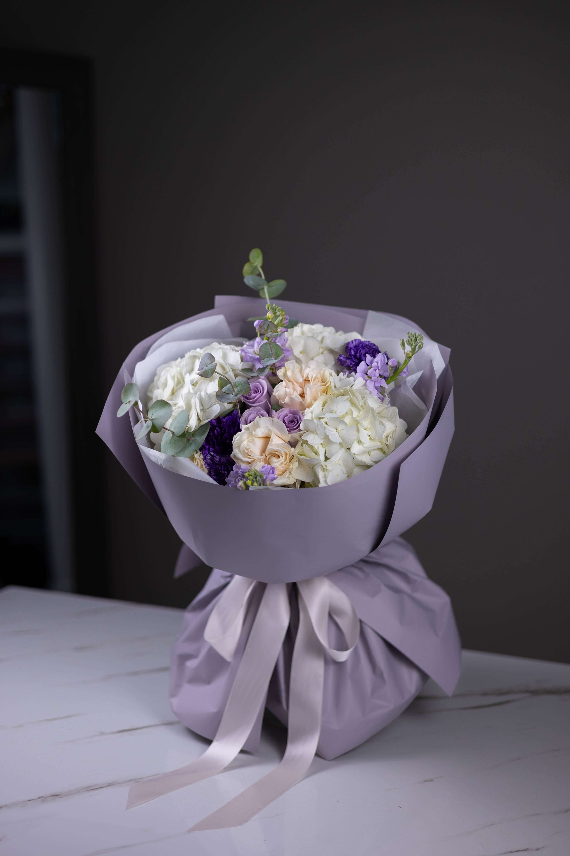 Bouquet of flowers wrapped in purple paper with a white ribbon on a dark background