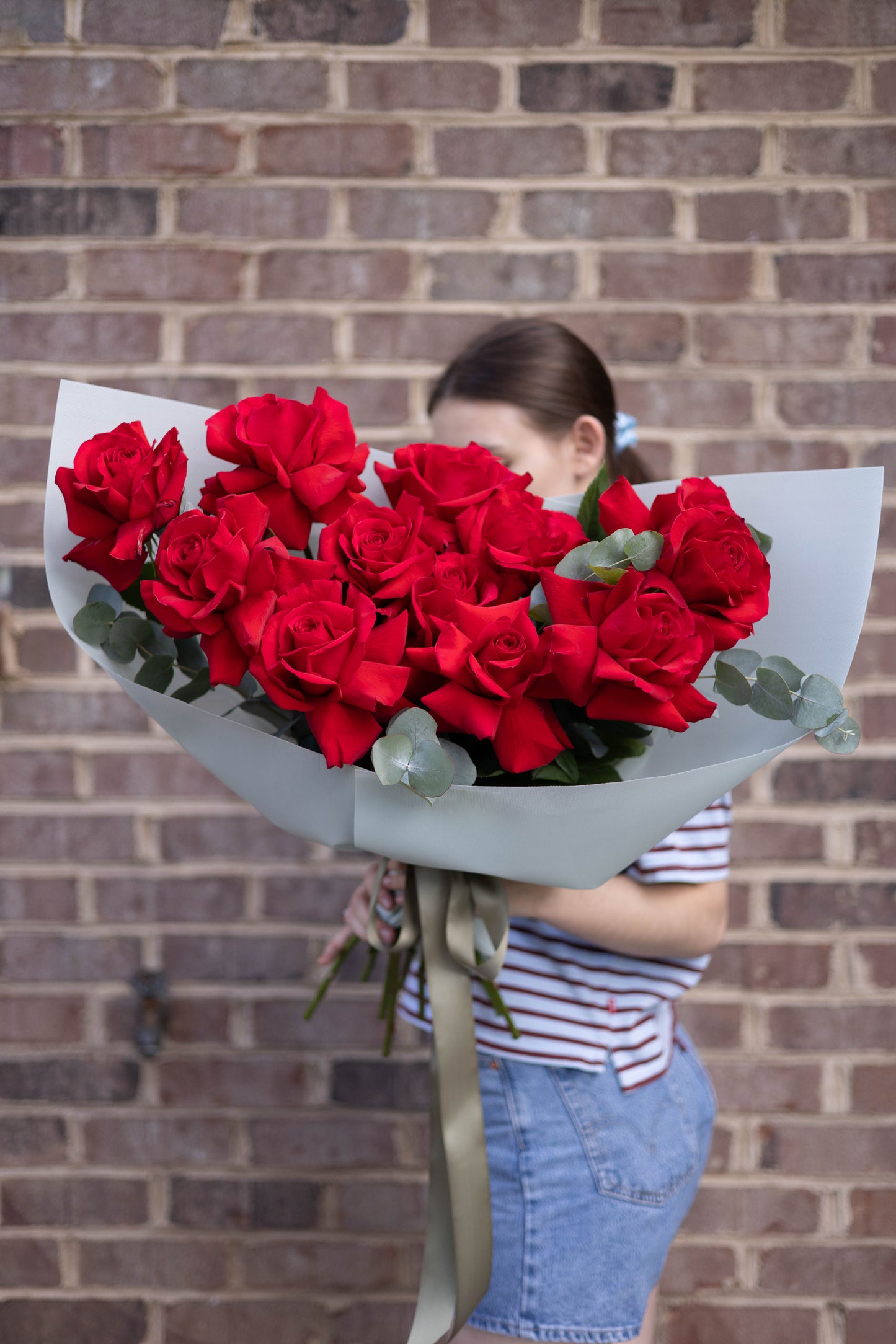 Person holding a large bouquet of red roses against a brick wall.