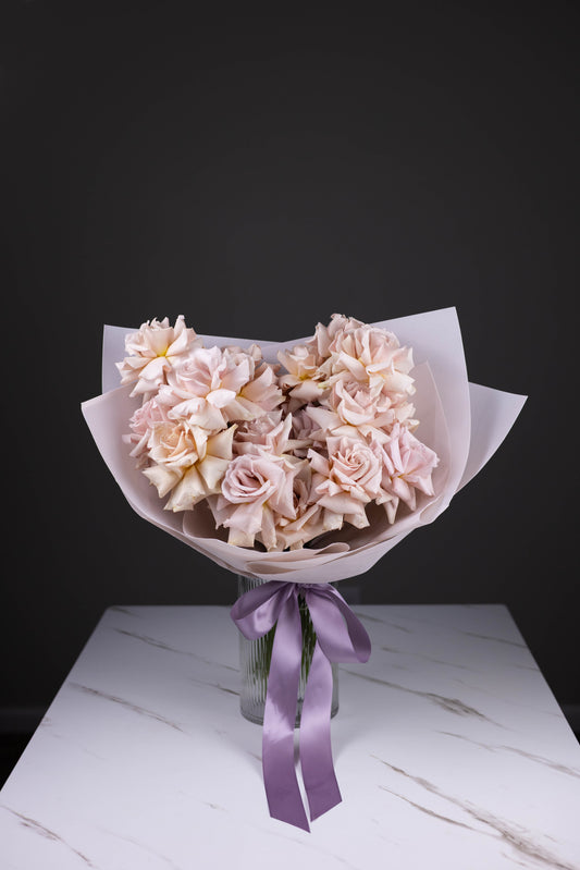 Bouquet of pink flowers with a purple ribbon on a marble surface against a black background
