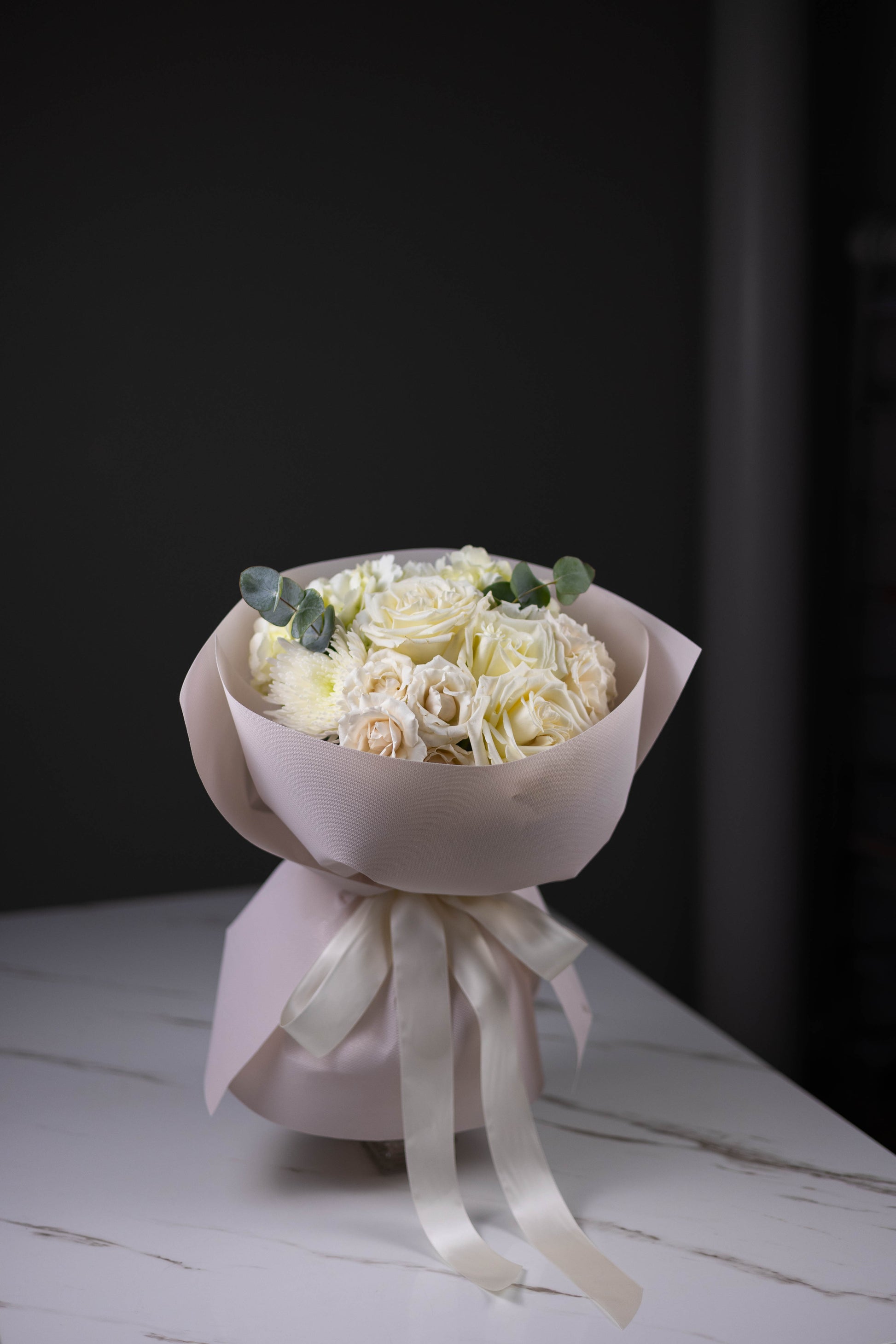 Bouquet of white flowers wrapped in pink paper with a white ribbon on a dark background