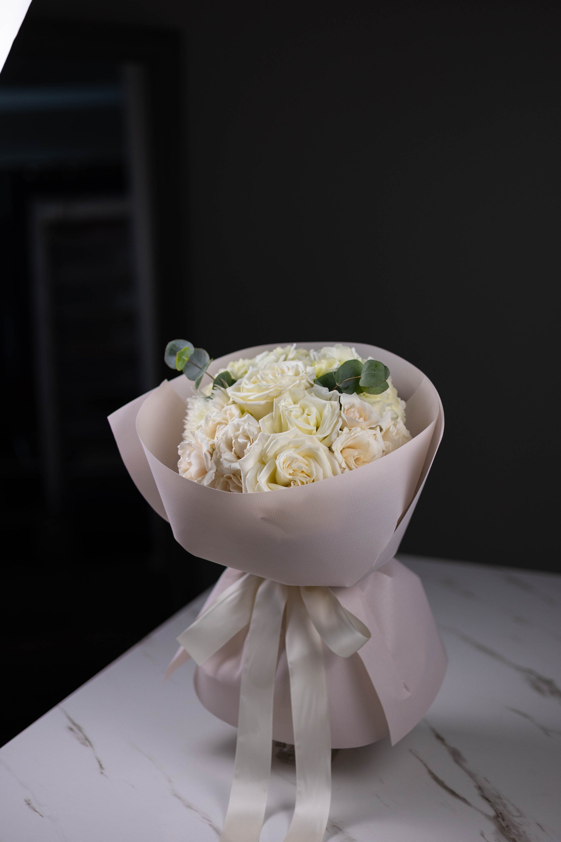 Bouquet of white flowers wrapped in paper with a ribbon on a dark background