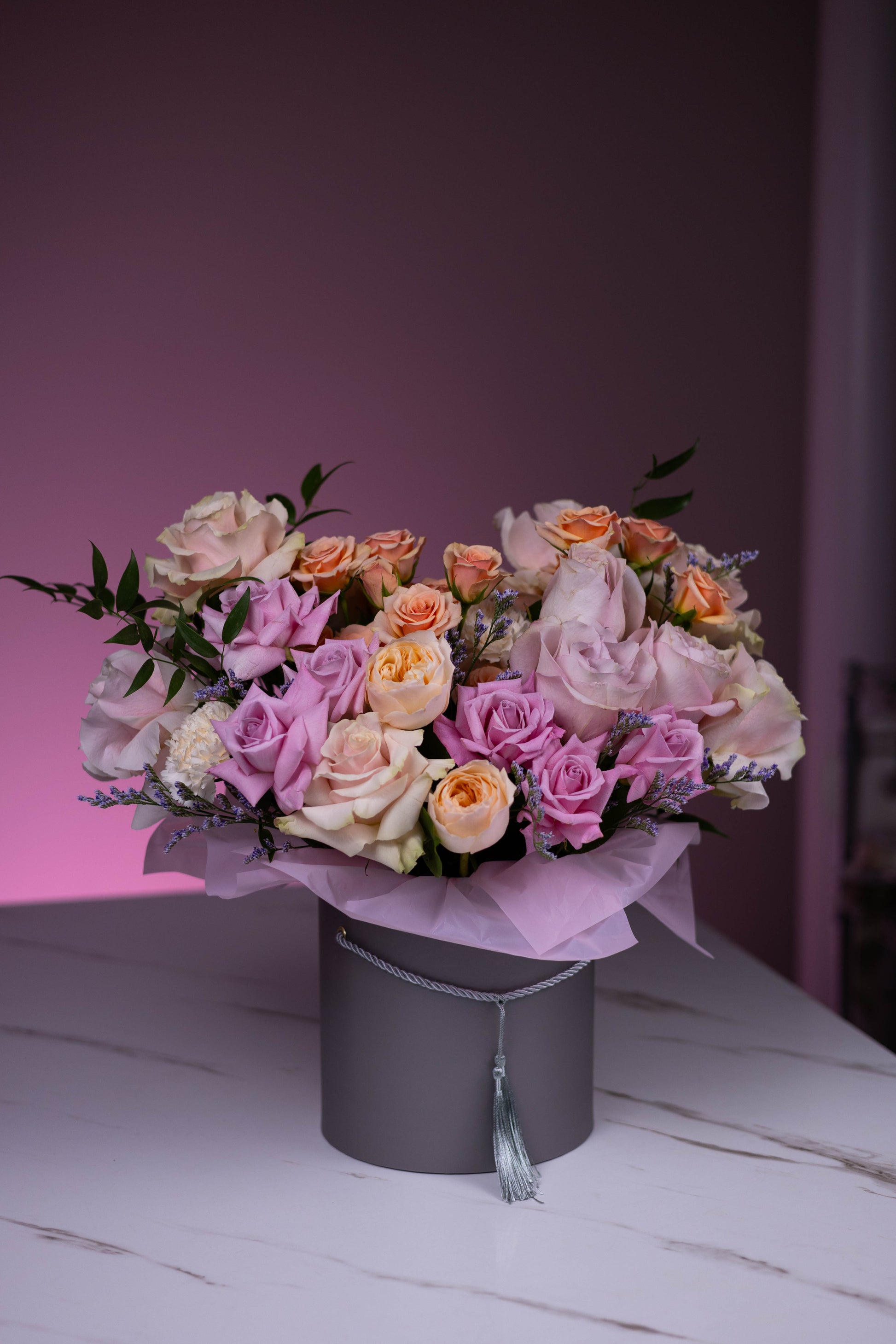 Bouquet of pink and orange flowers in a gray box on a white surface with a pink background