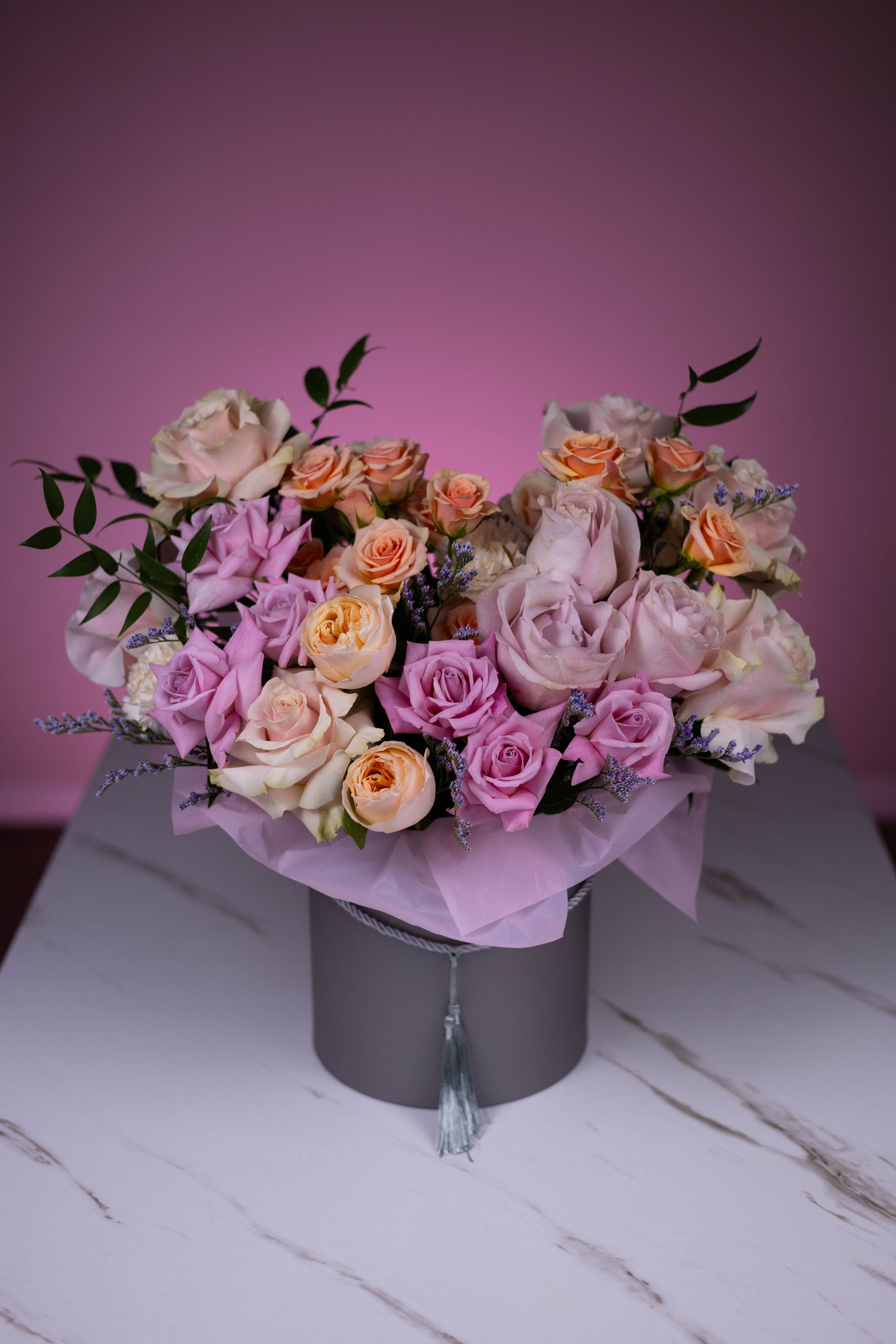 Bouquet of flowers in a gray box on a white surface with a pink background