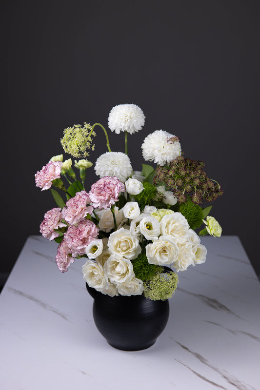White and blush floral centerpiece captured from a slight angle on white marble surface