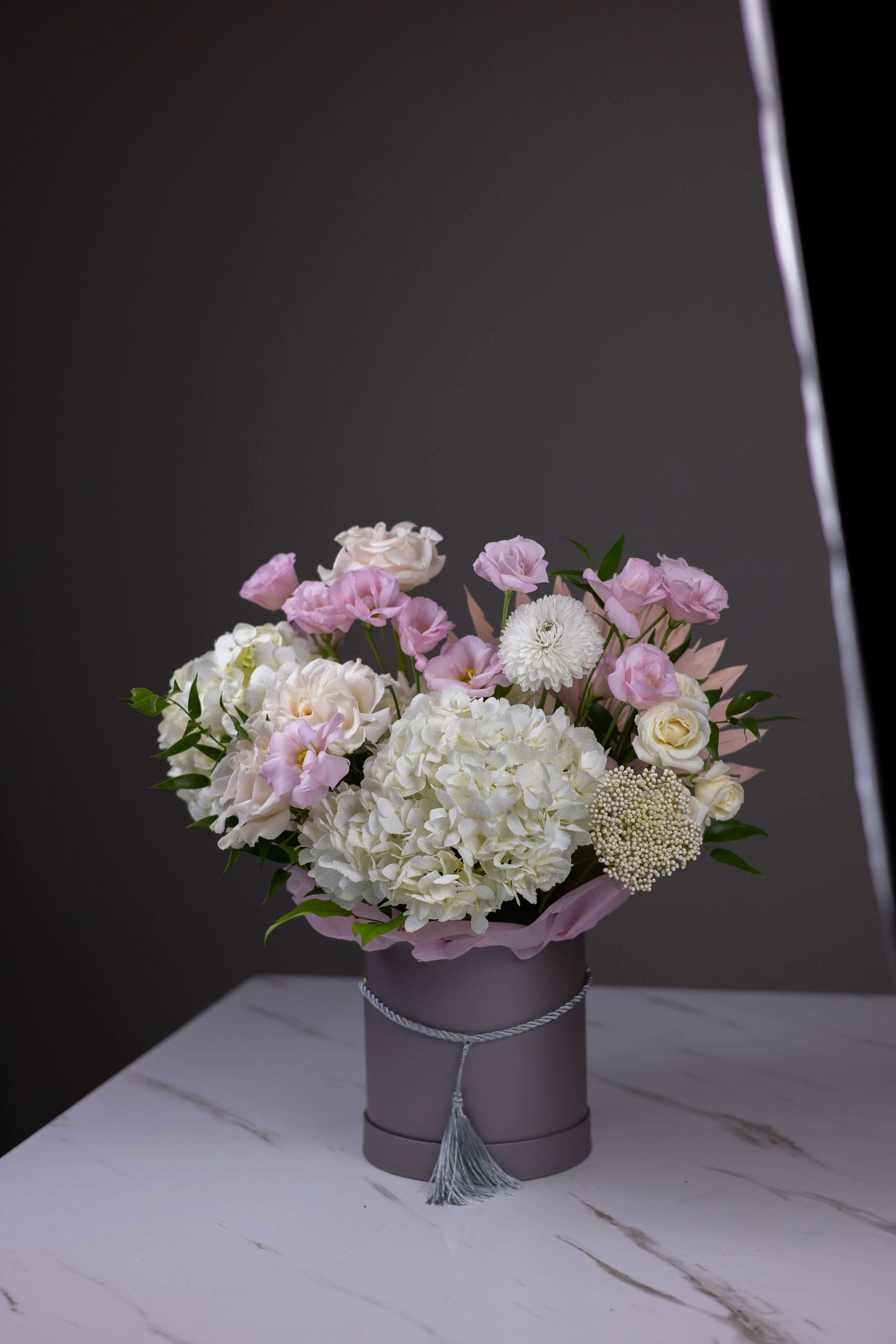 Bouquet of pink and white flowers in a gray vase on a marble surface with a dark background