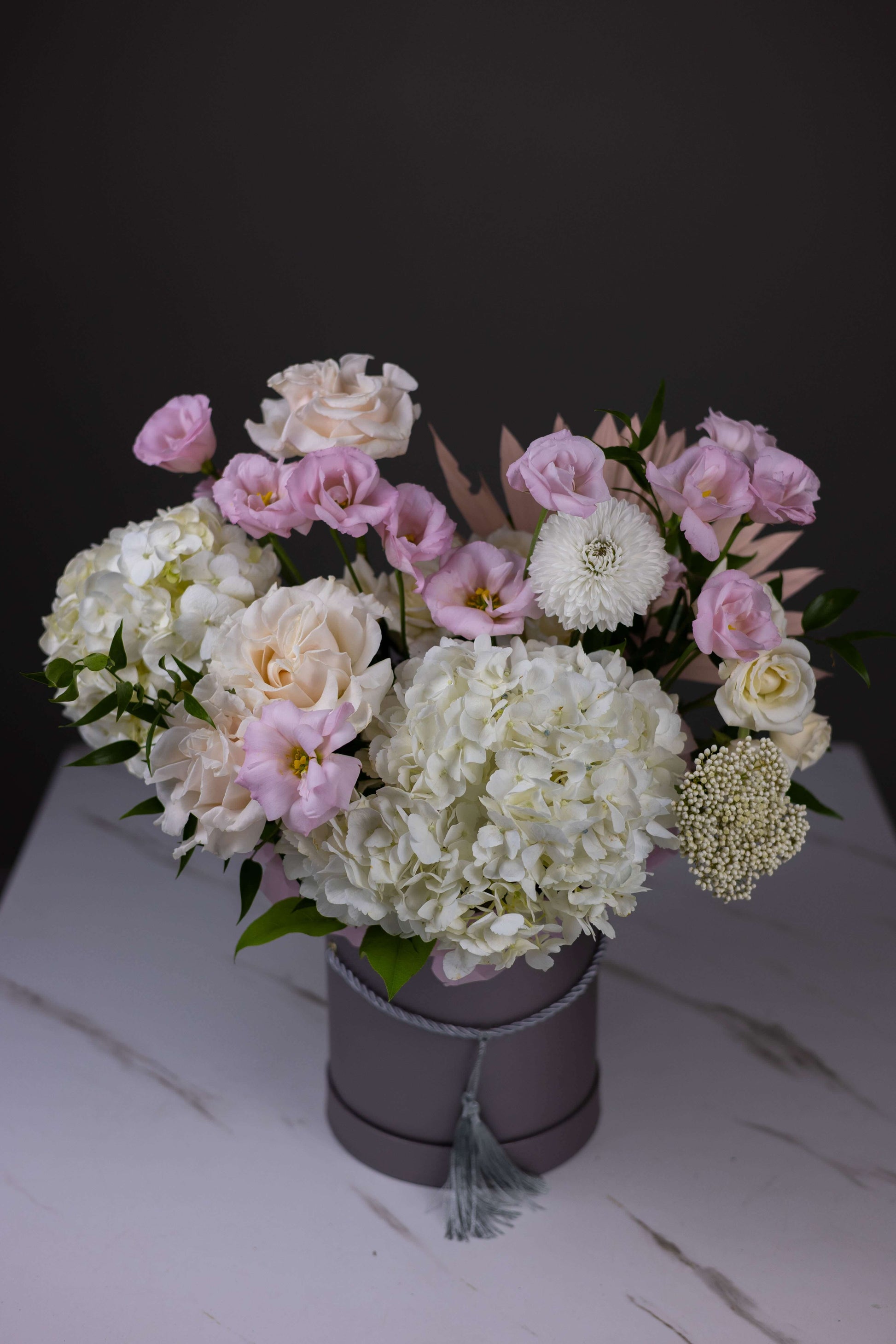 Bouquet of flowers in a gray container on a white surface with a dark background