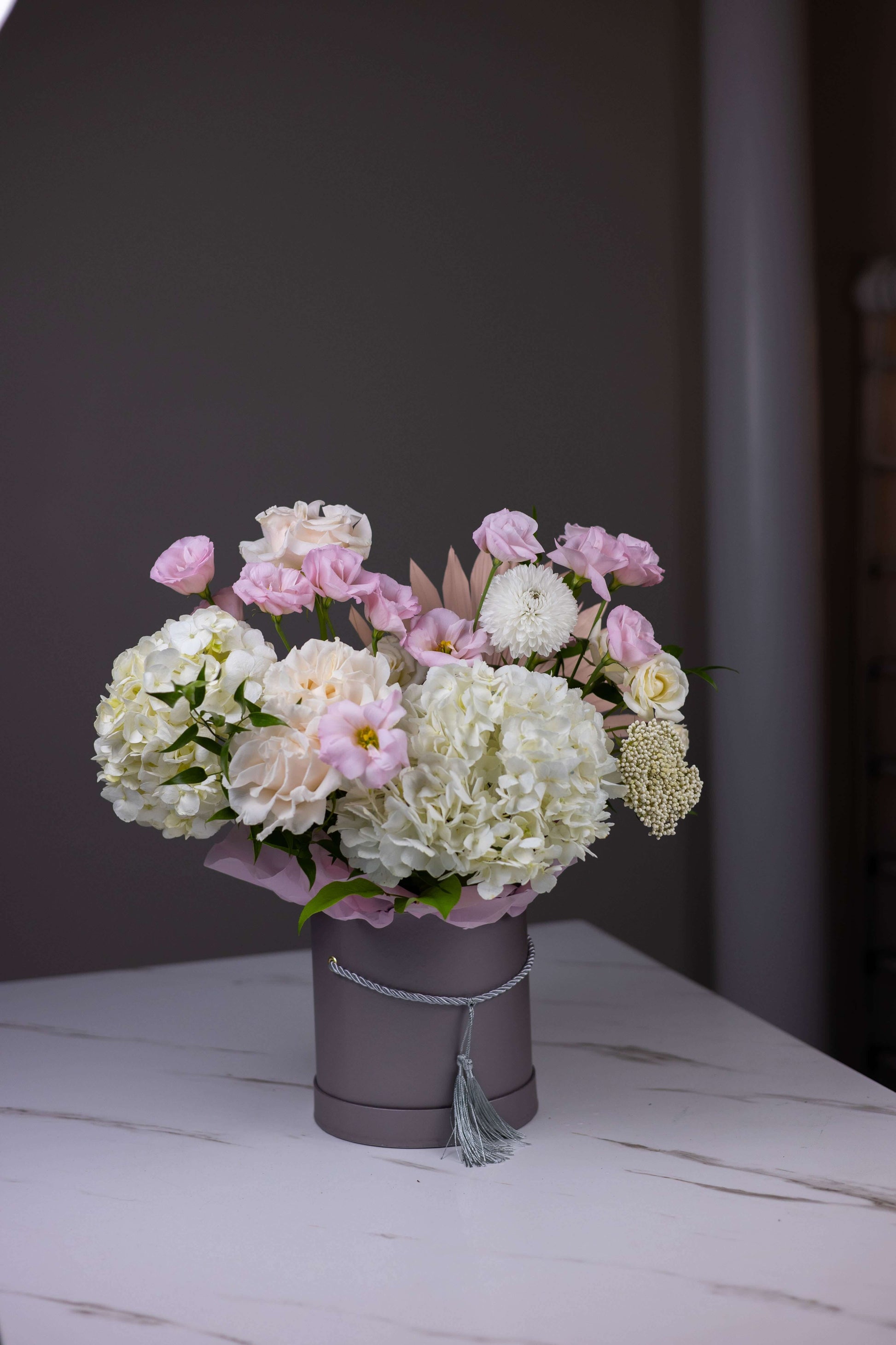 Bouquet of flowers in a gray pot on a white surface with a dark background