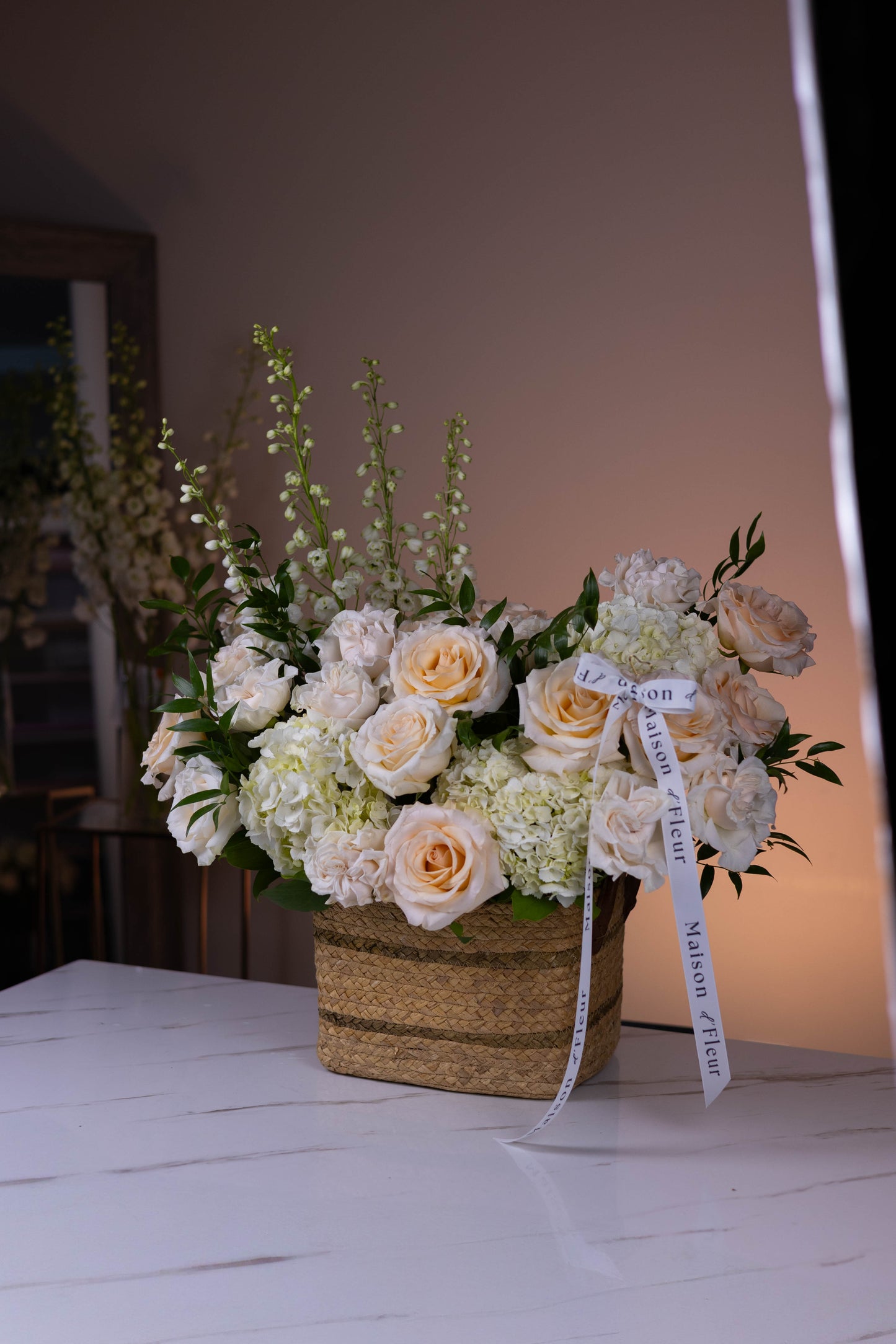 Floral arrangement with white and yellow flowers in a woven basket on a white surface.