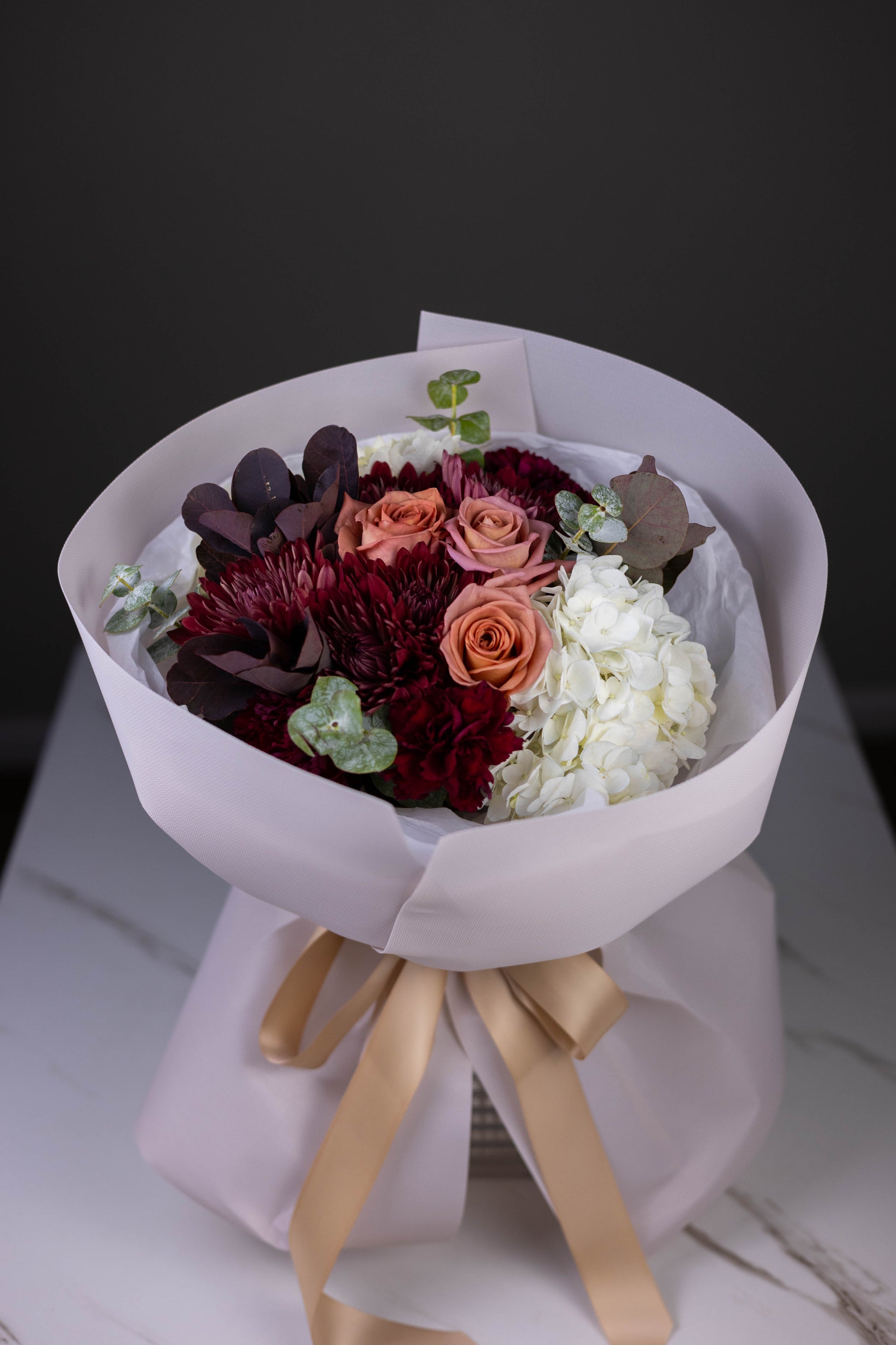 Bouquet of flowers wrapped in white paper with a gold ribbon on a dark background