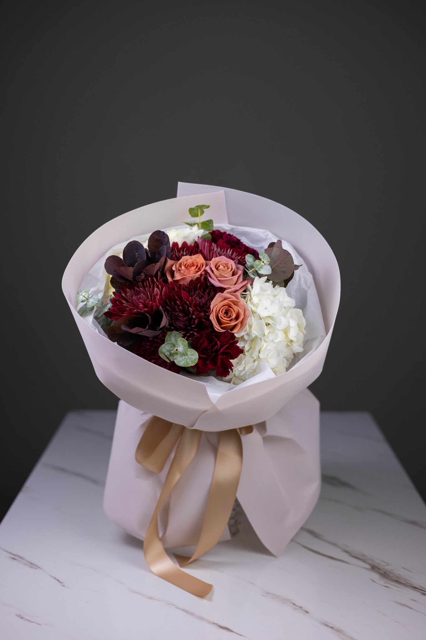 Bouquet of flowers wrapped in white paper with a gold ribbon on a wooden surface.