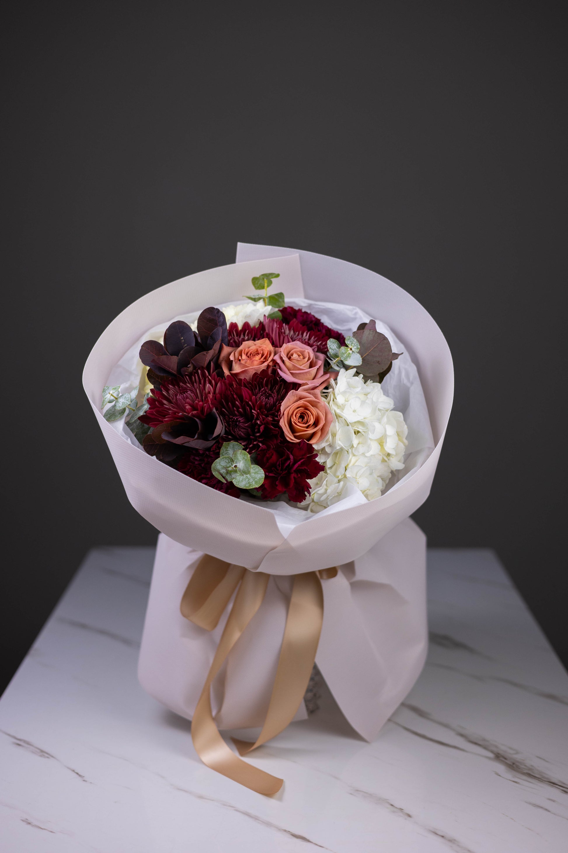 Bouquet of flowers wrapped in white paper with a gold ribbon on a wooden surface.