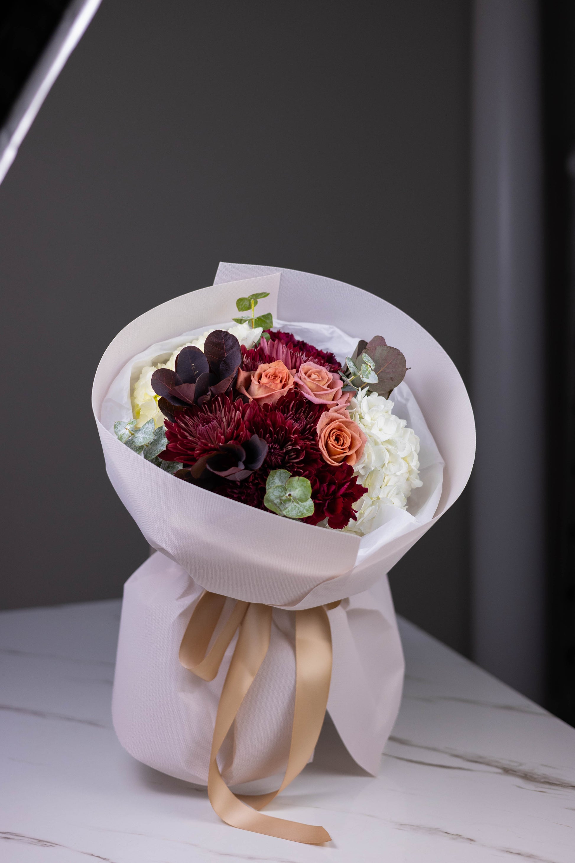 Bouquet of flowers wrapped in white paper with a gold ribbon on a dark background