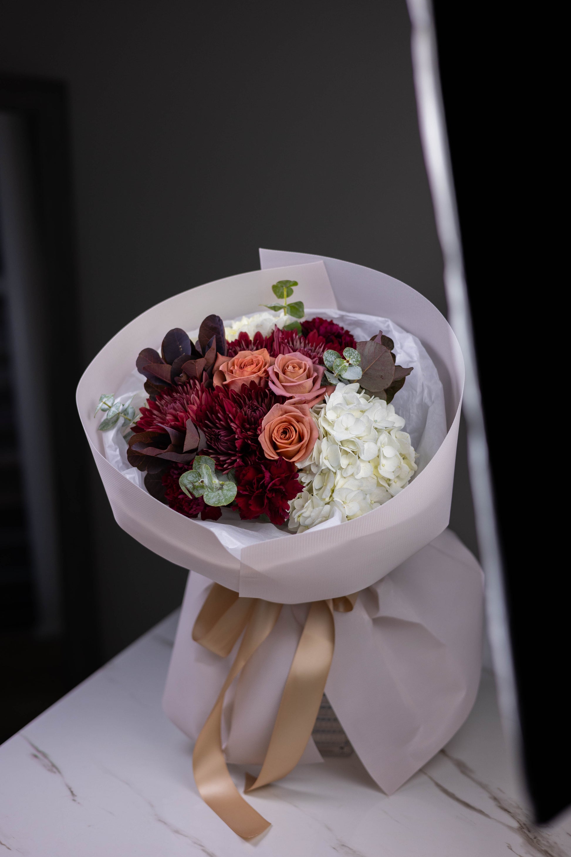Bouquet of flowers wrapped in white paper with a gold ribbon on a dark background