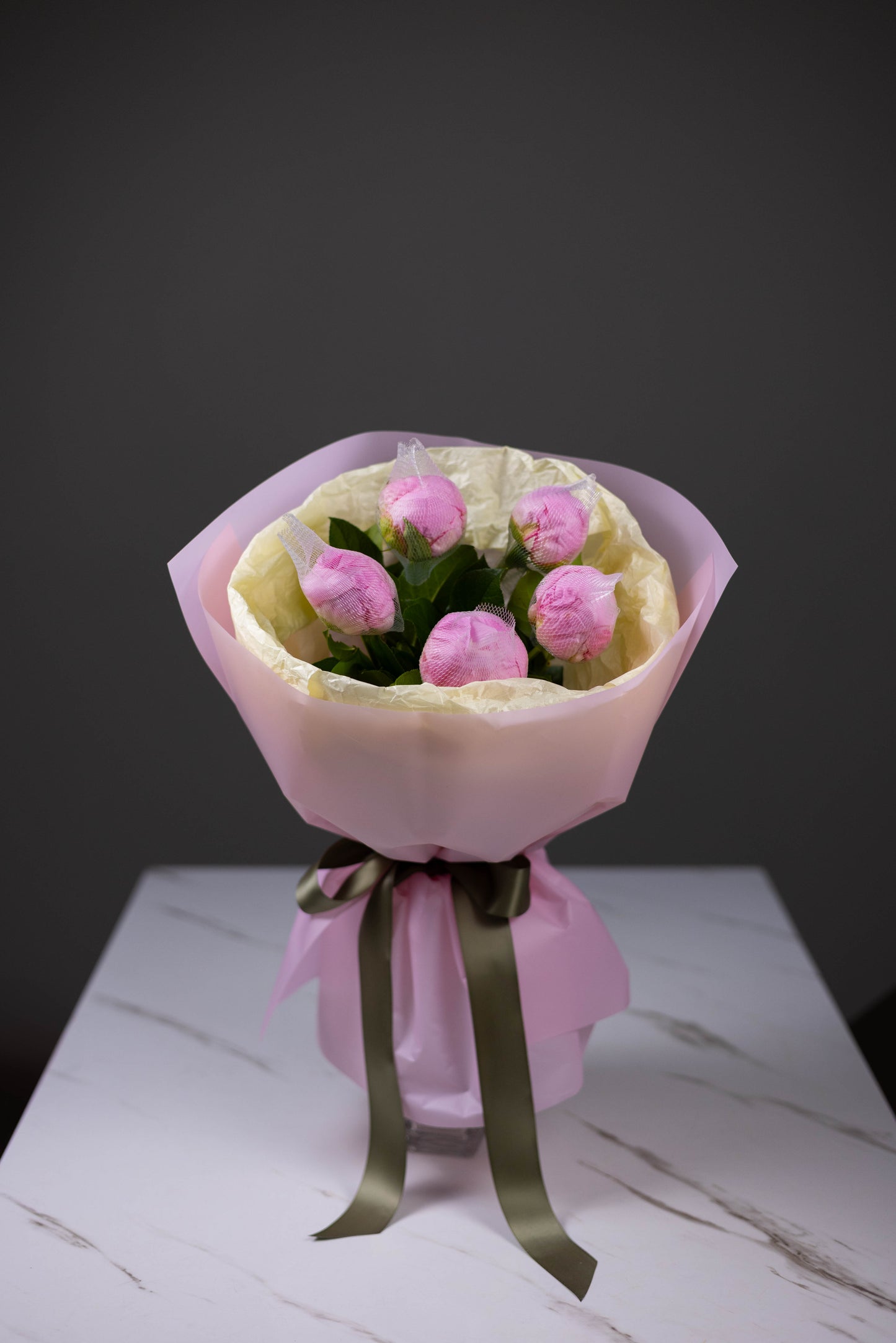 Bouquet of pink peonies wrapped in pink paper with a green ribbon on a white surface.