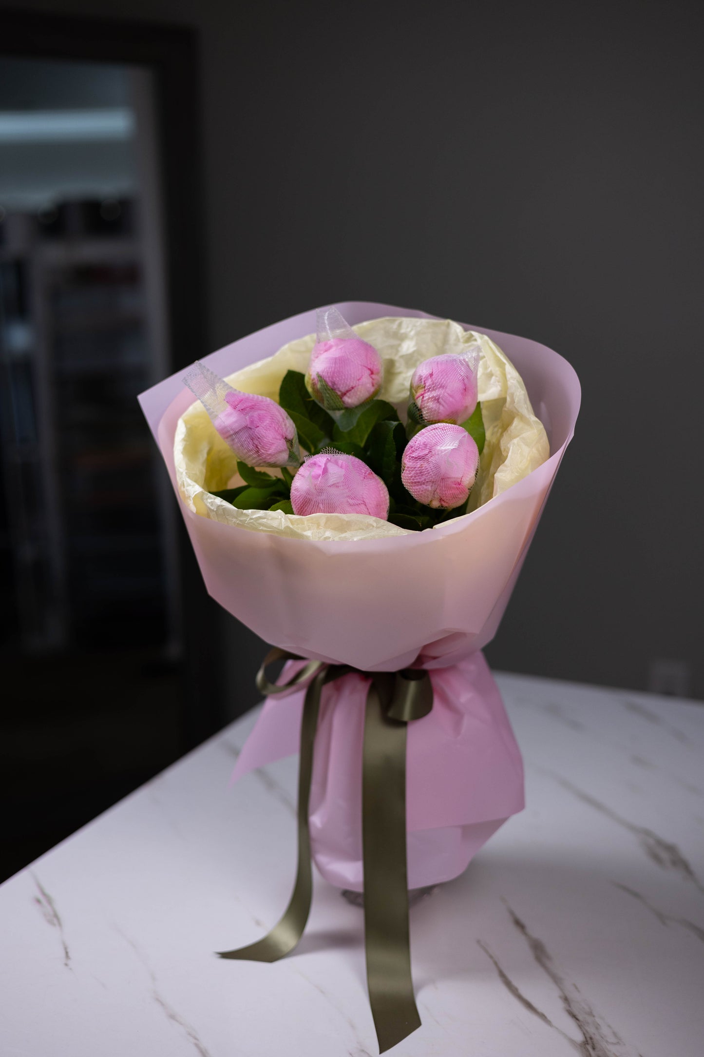 Bouquet of pink flowers wrapped in pink paper with a green ribbon on a marble surface.
