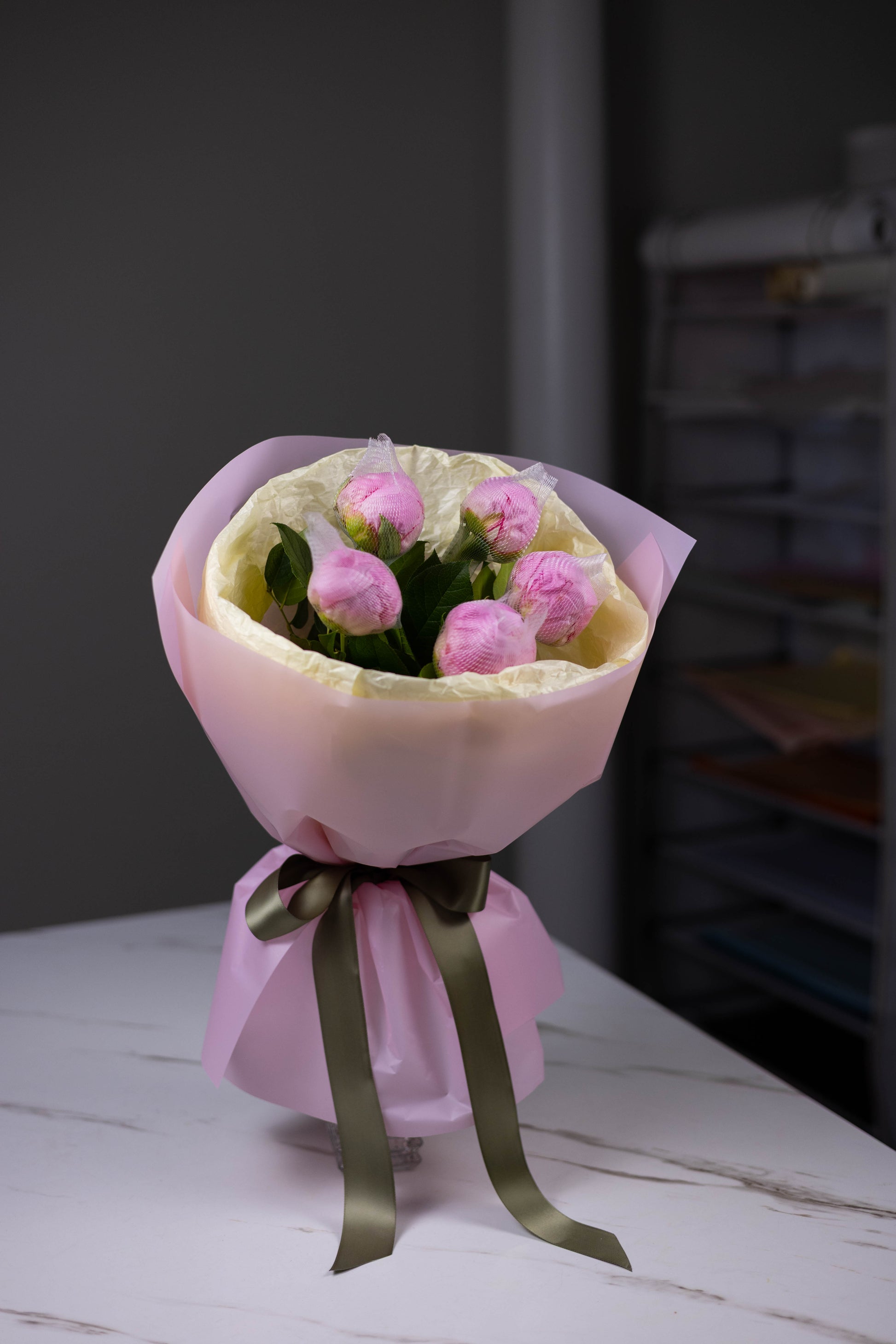 Bouquet of pink flowers wrapped in pink paper with a green ribbon on a white surface.