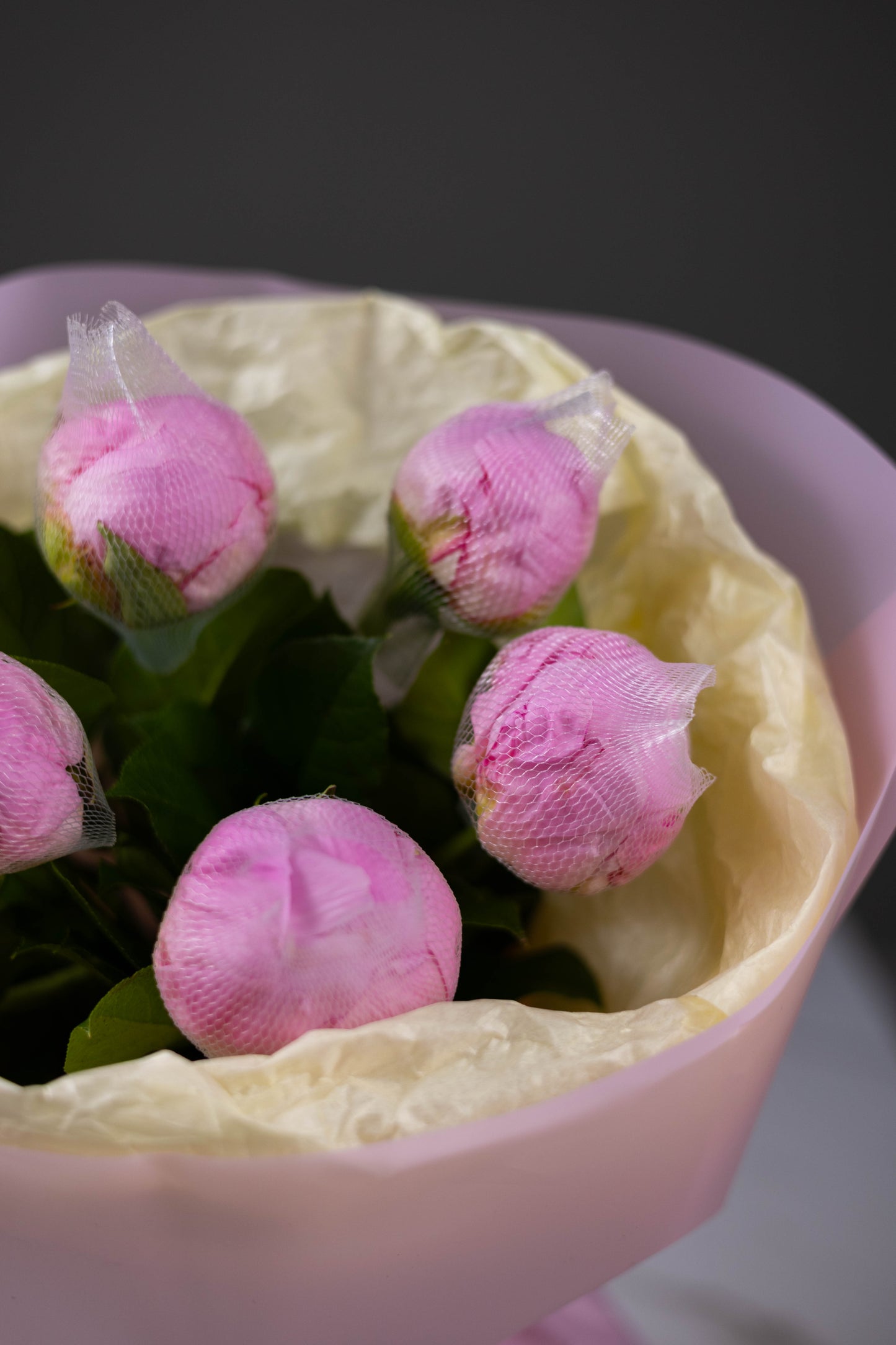 Pink flowers wrapped in tissue paper inside a decorative pink bowl with a blurred background