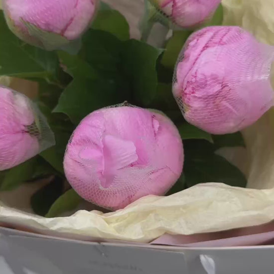 Close-up of pink peony buds wrapped in mesh netting in a luxury floral bouquet